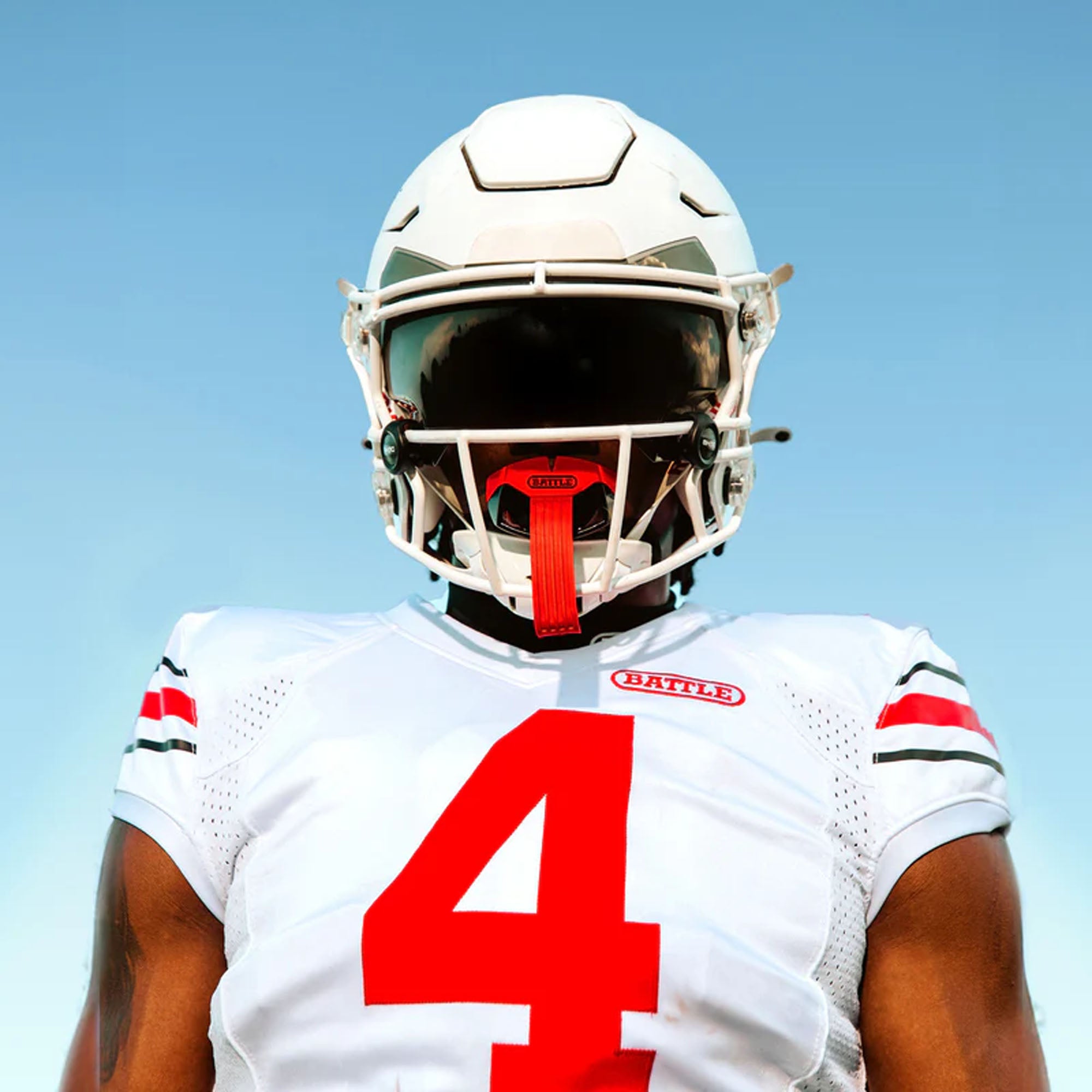 Person wearing a football mouthguard helmet and jersey with number 4 against a clear blue sky