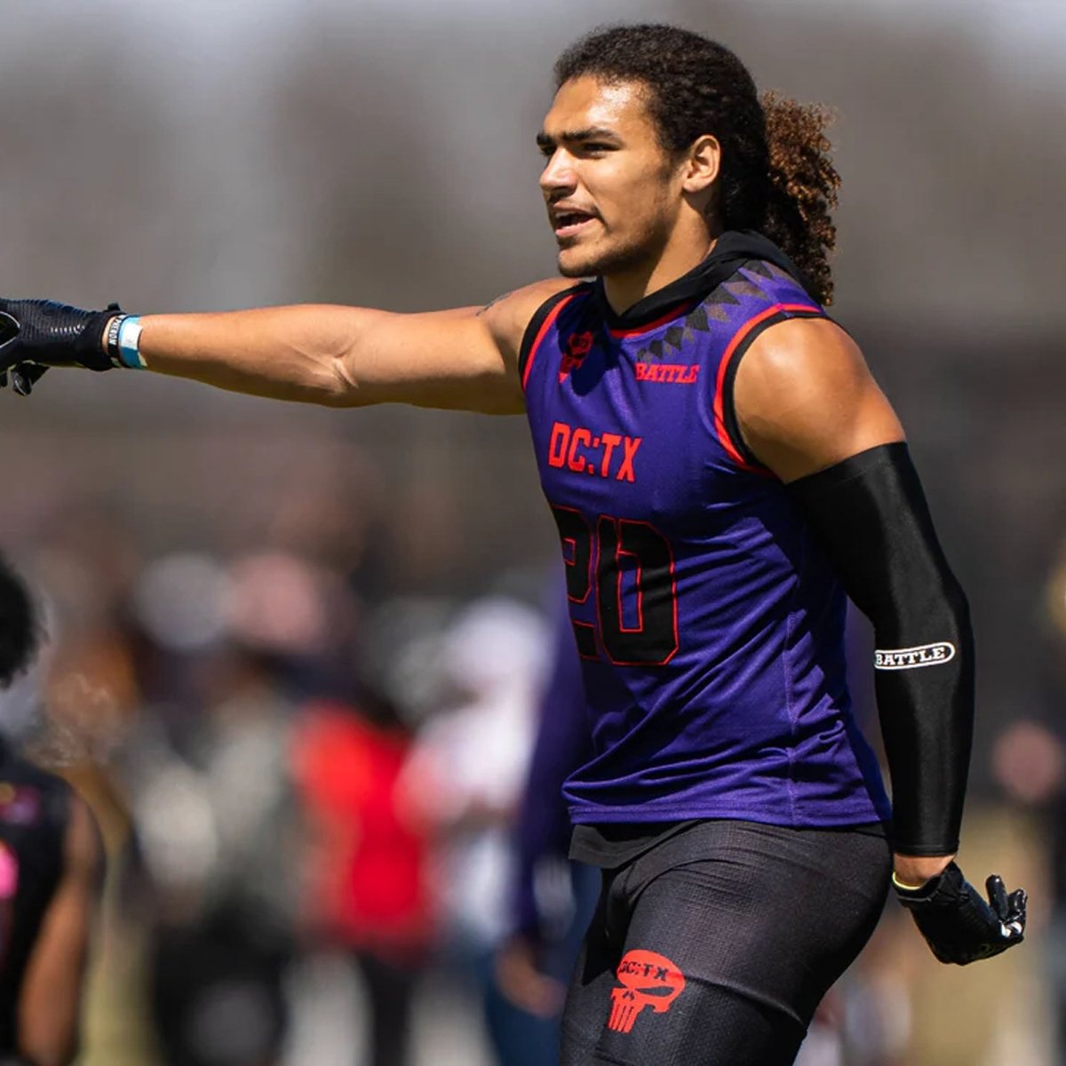 Athlete in a purple jersey with red text and football full arm sleeves on a sports field