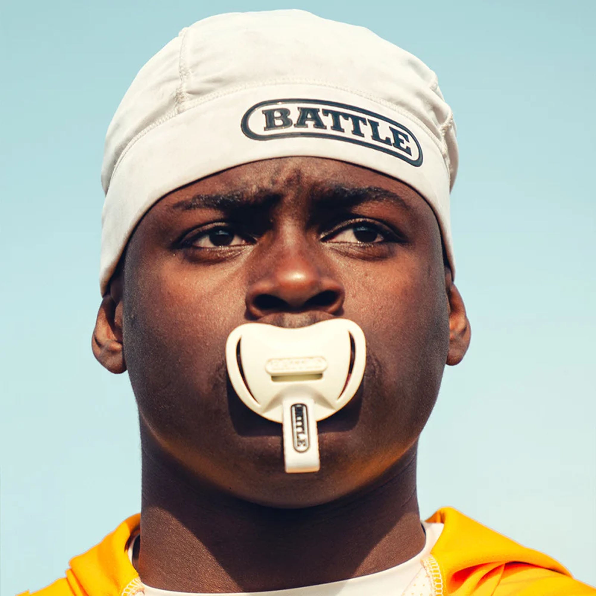Person wearing a pro skull cap headband with 'BATTLE' text and a white object in their mouth against a clear blue sky.