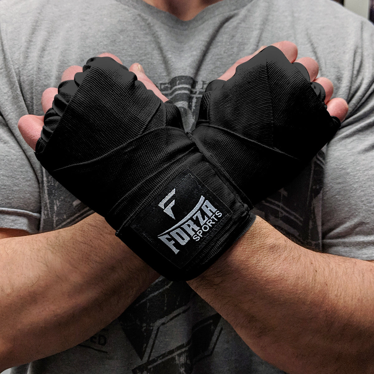 Person wearing black boxing wraps with Forza Sports logo on a gray shirt background