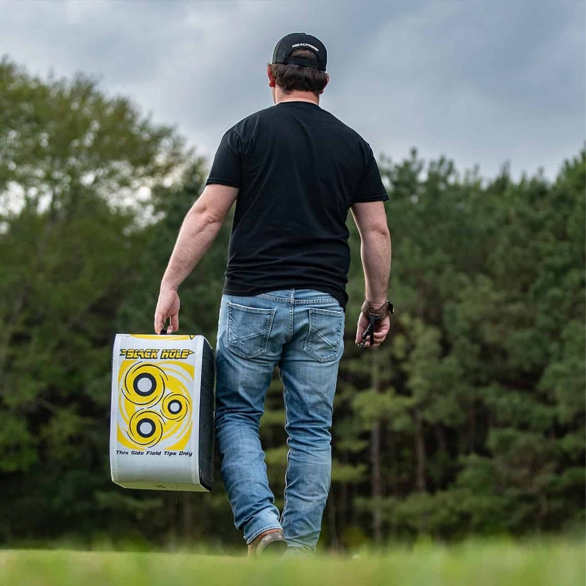 Man walking outdoors carrying a large archery target with a logo on it.
