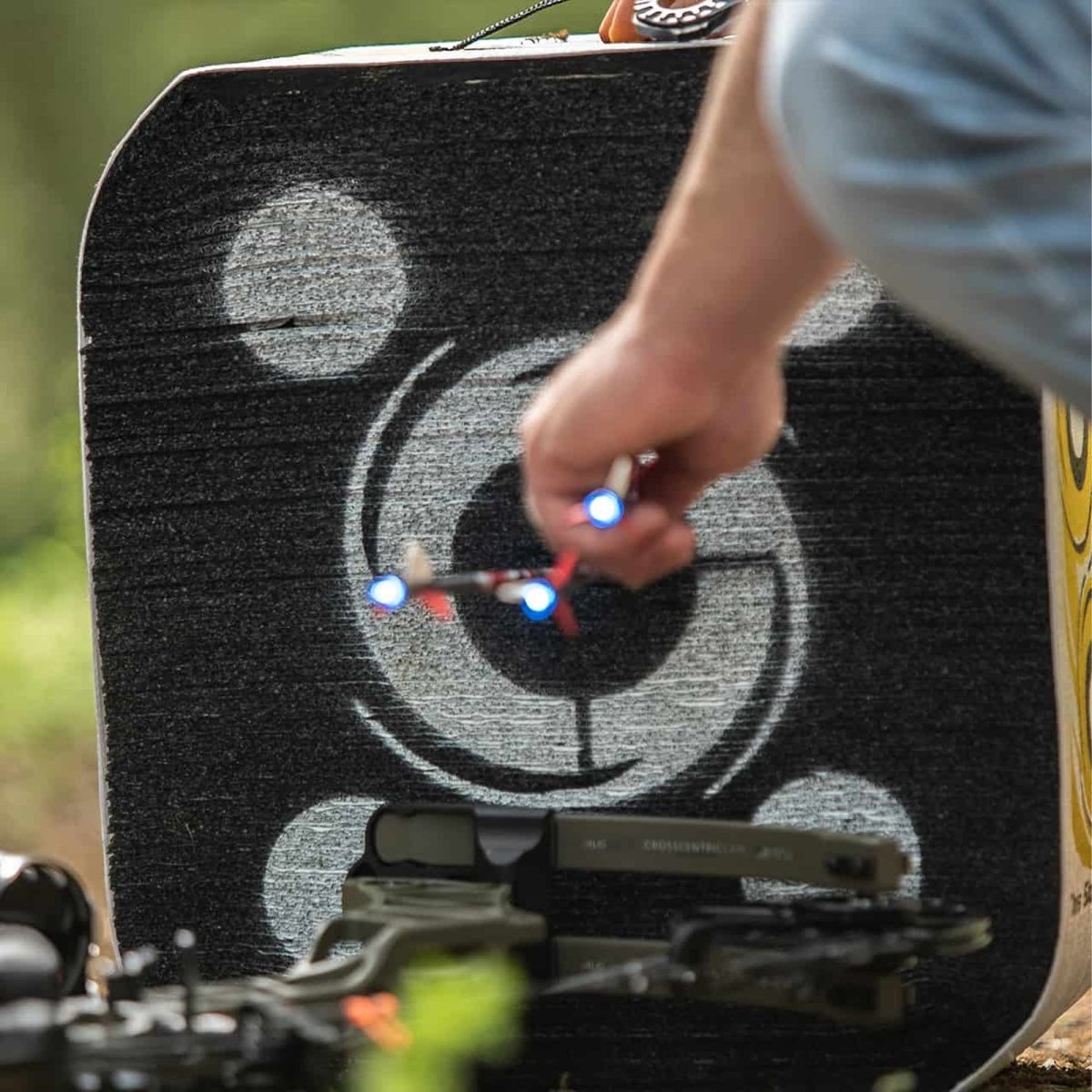 Person aiming a bow and arrow at a archery target with a visible brand logo.