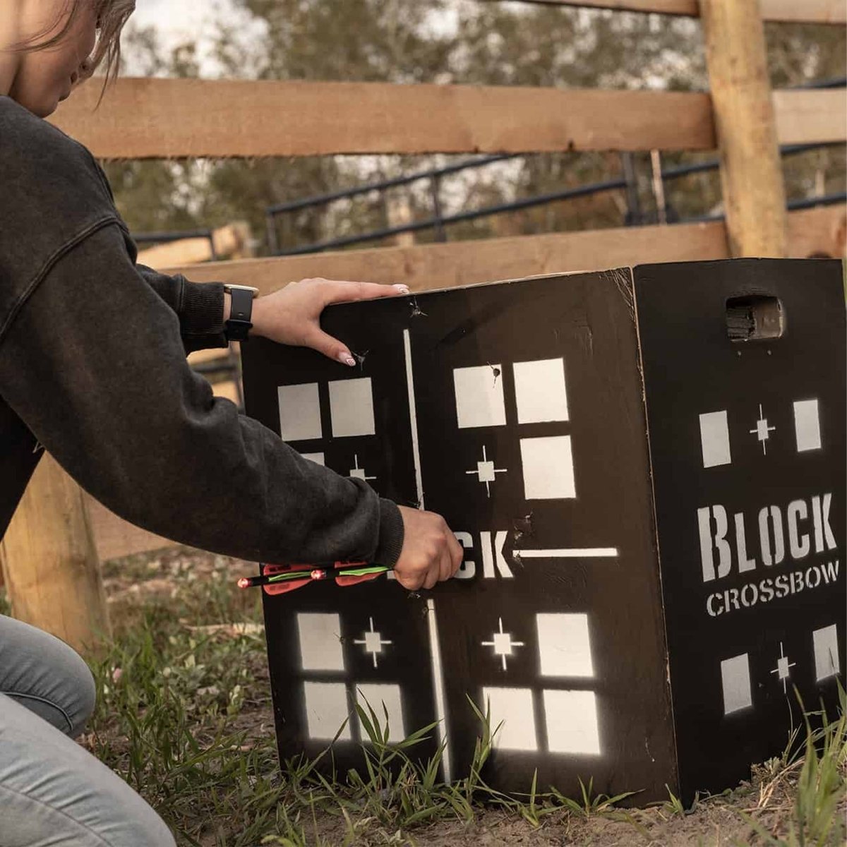 Person interacting with a crossbow 6-sided foam archery target labeled 'Block Crossbow' outdoors.