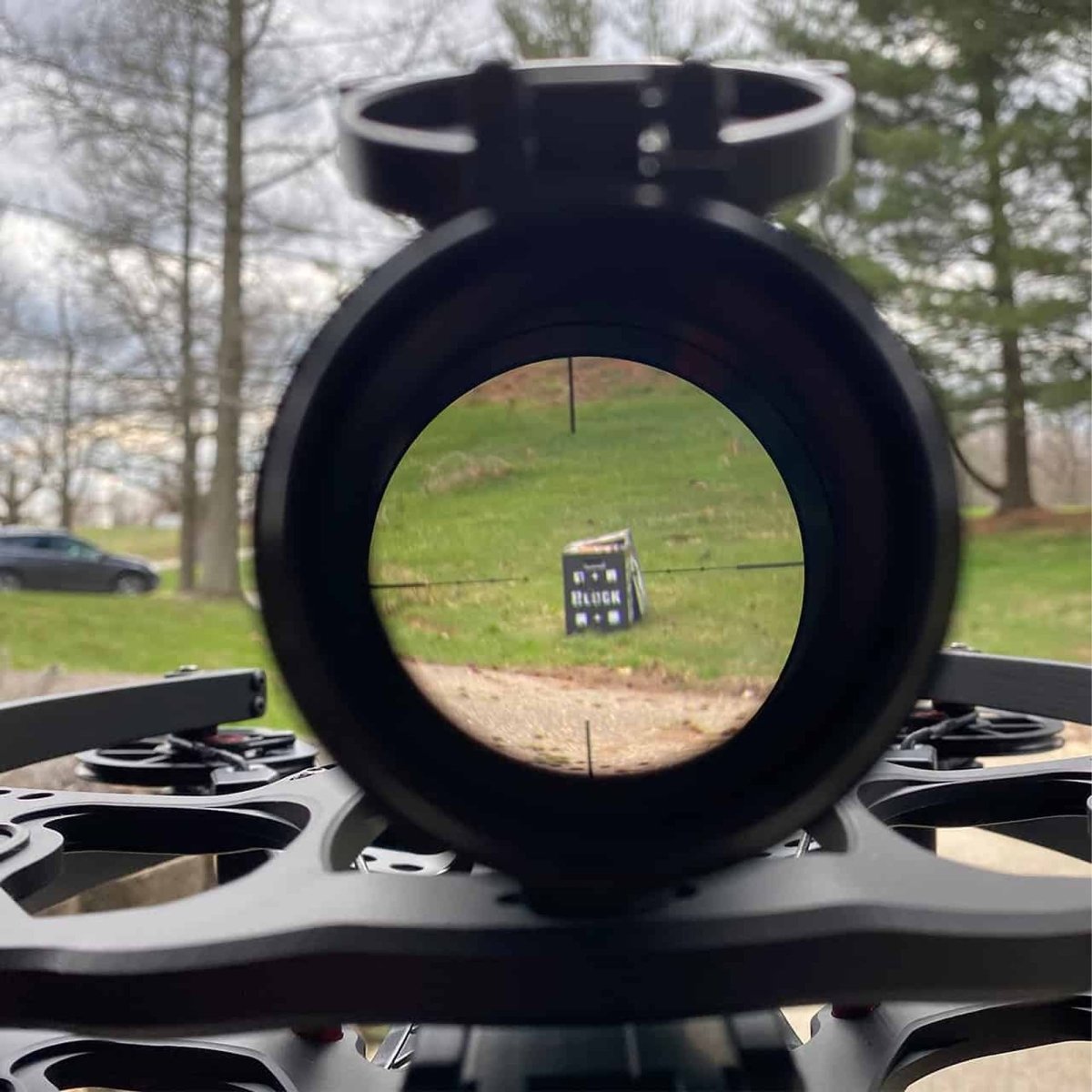 Scopes on a stand infinity crossbow with a view through the lens towards a grassy field and trees.