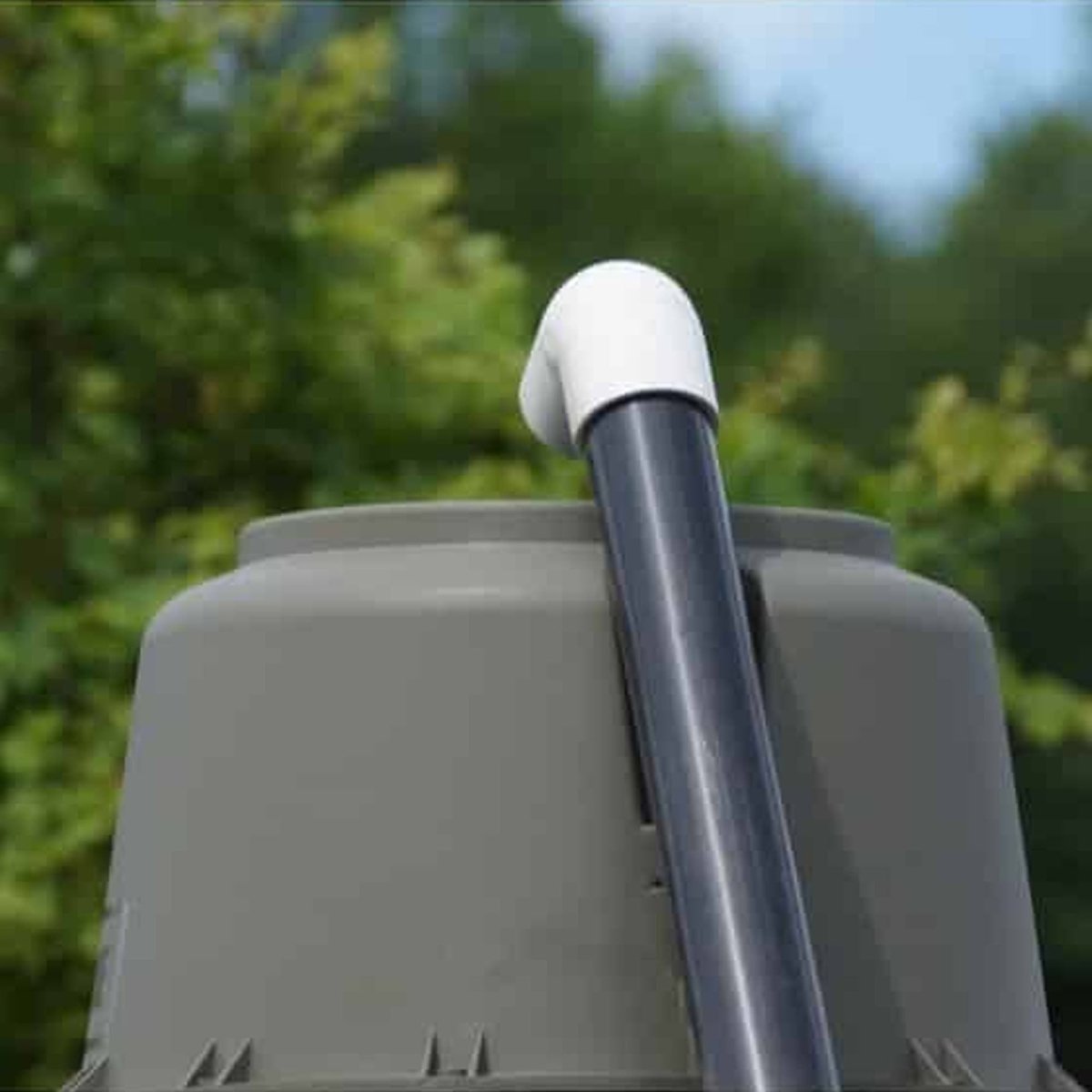 Gray plastic container feeder filler with a white handle and black rod against a blurred green outdoor background