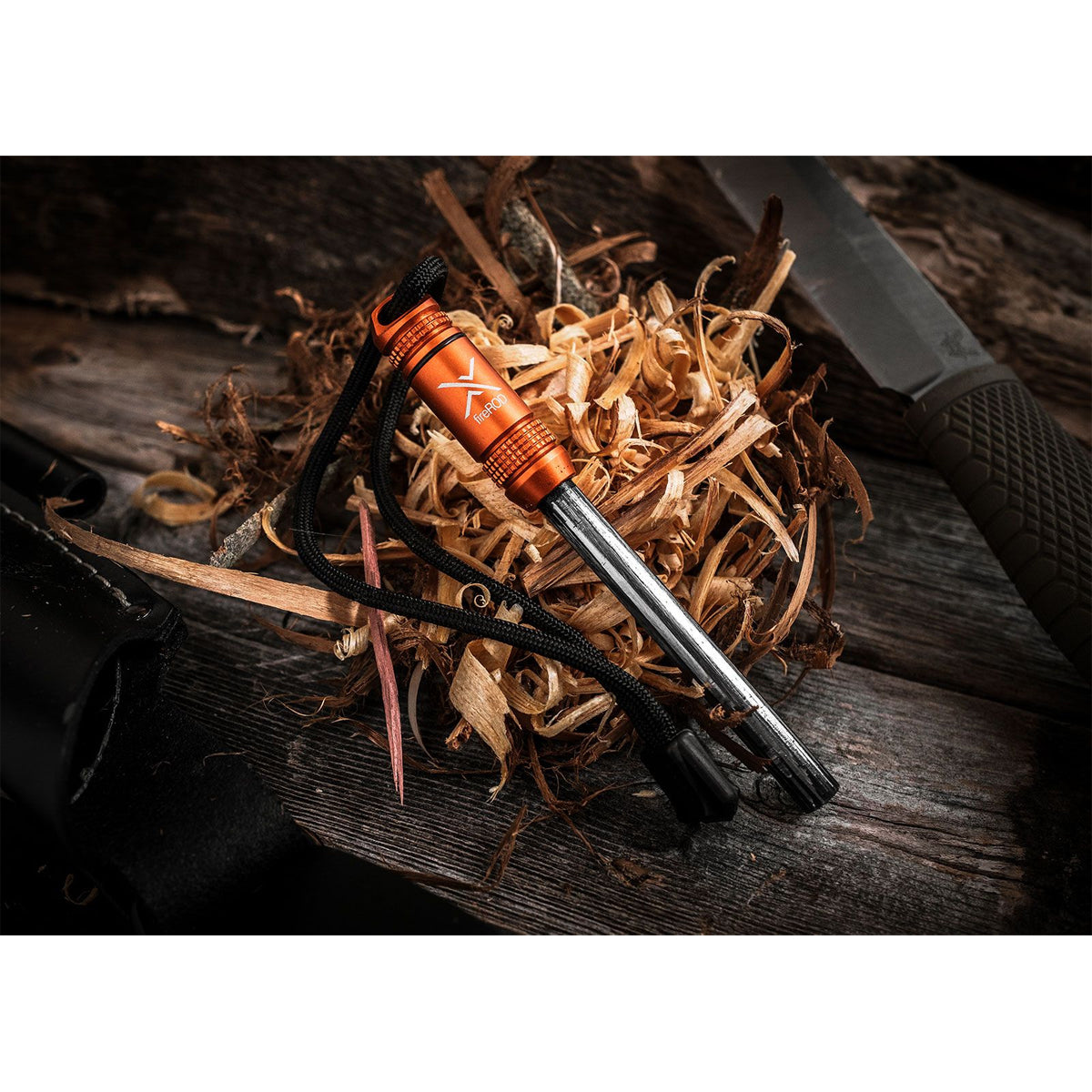 Fire starter with orange handle and metal striker on wood and twigs