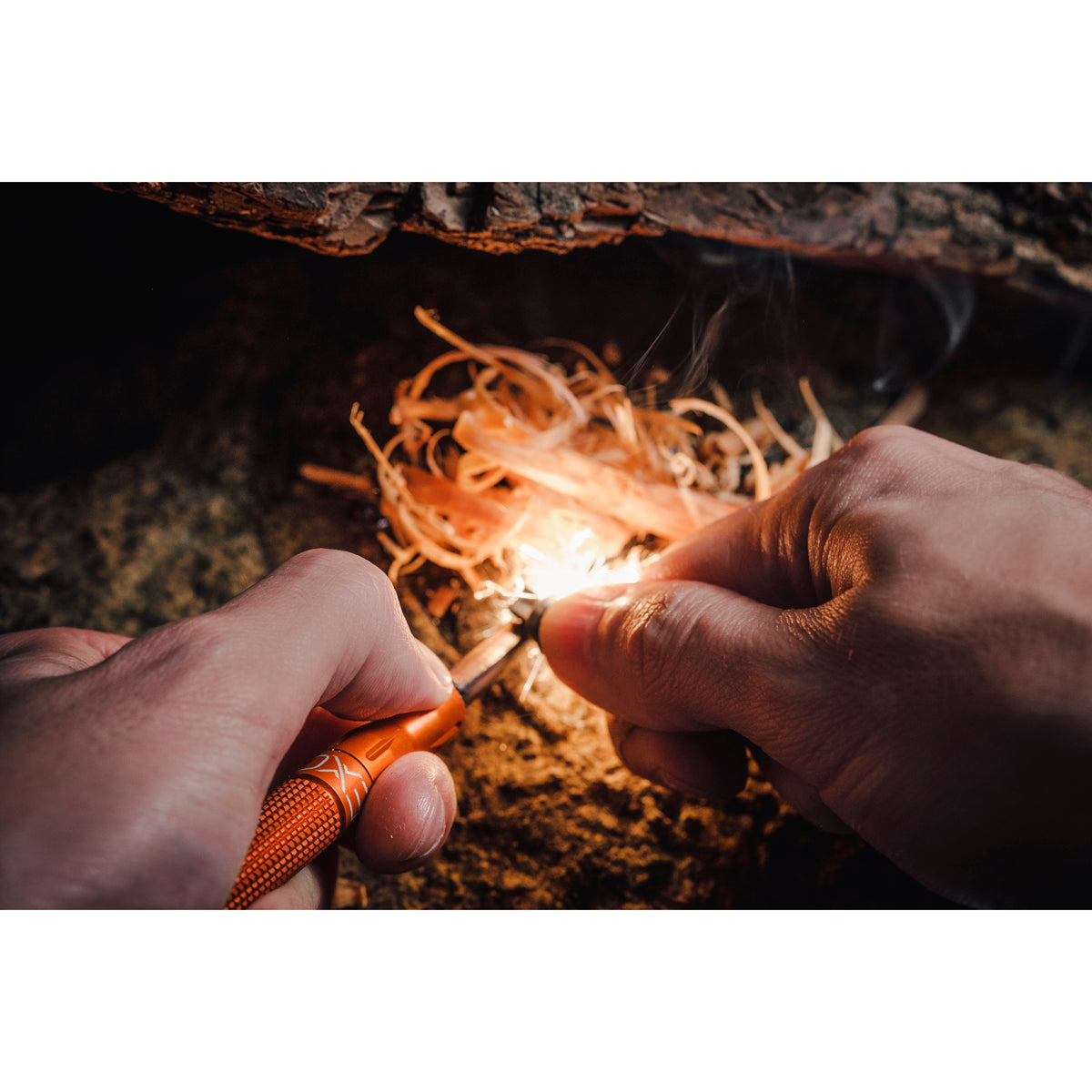 Person using a fire starter to ignite dry grass with a close-up focus on the hands and tool.