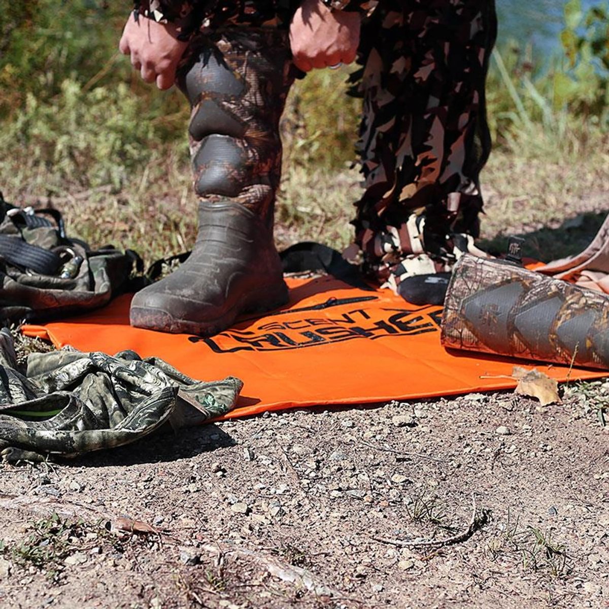 Person wearing camouflage boots on an orange mat bag with 'Scout' branding in a natural setting.
