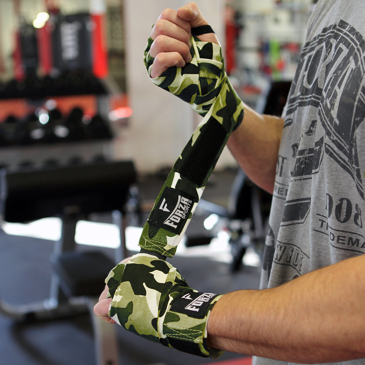 Person wearing green camouflage boxing hand wraps with Fostex branding in a gym setting.