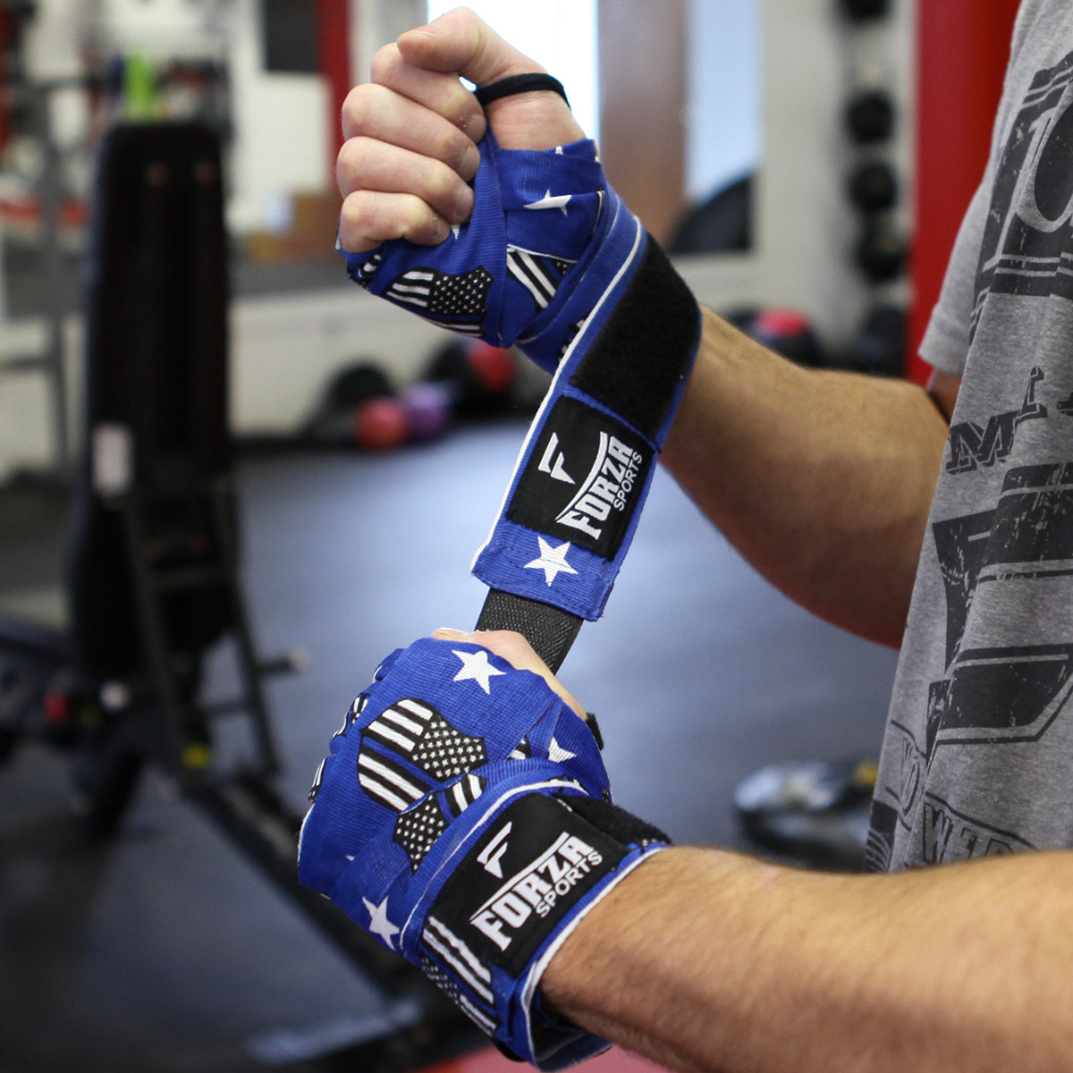 Person wearing blue boxing gloves with star and stripe design, wrapped with black wrist wraps, in a gym setting.