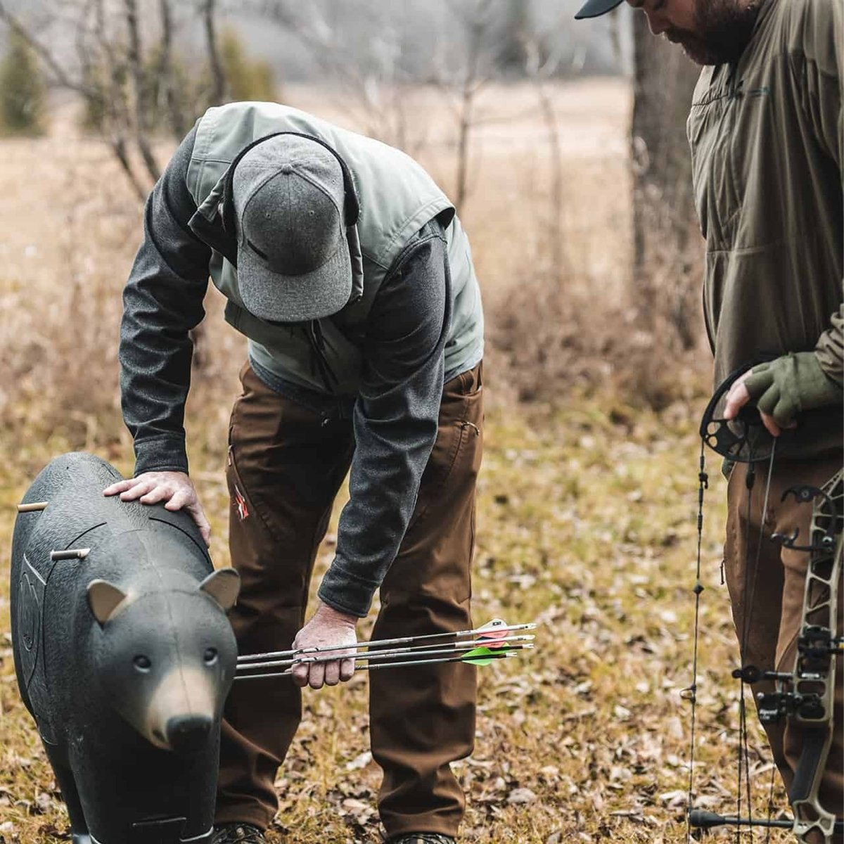 Two hunters with 3d bear archery target in a field, one holding a bear target.