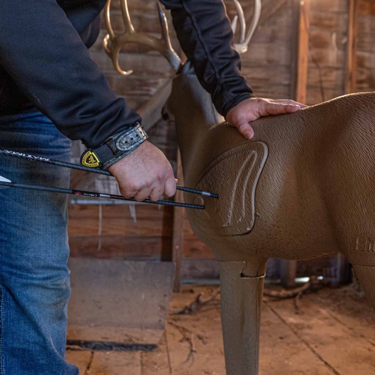 Person adjusting a brown deer shaped 3d archery target saddle on an animal, likely in a barn setting.