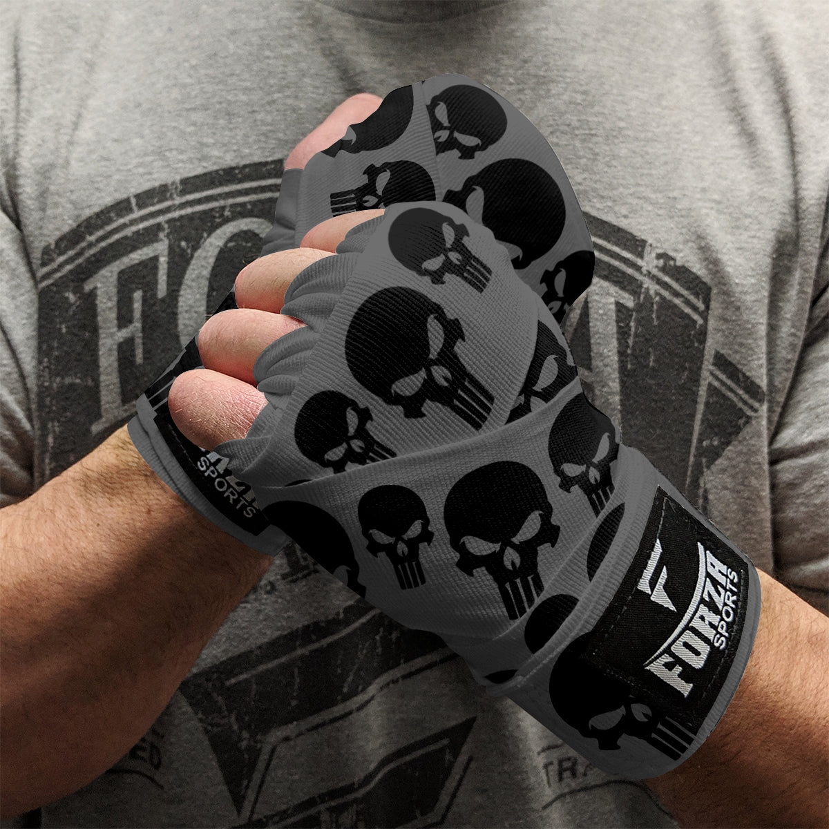 Gray boxing hand wraps with black skull patterns worn by a person, against a gray t-shirt background.