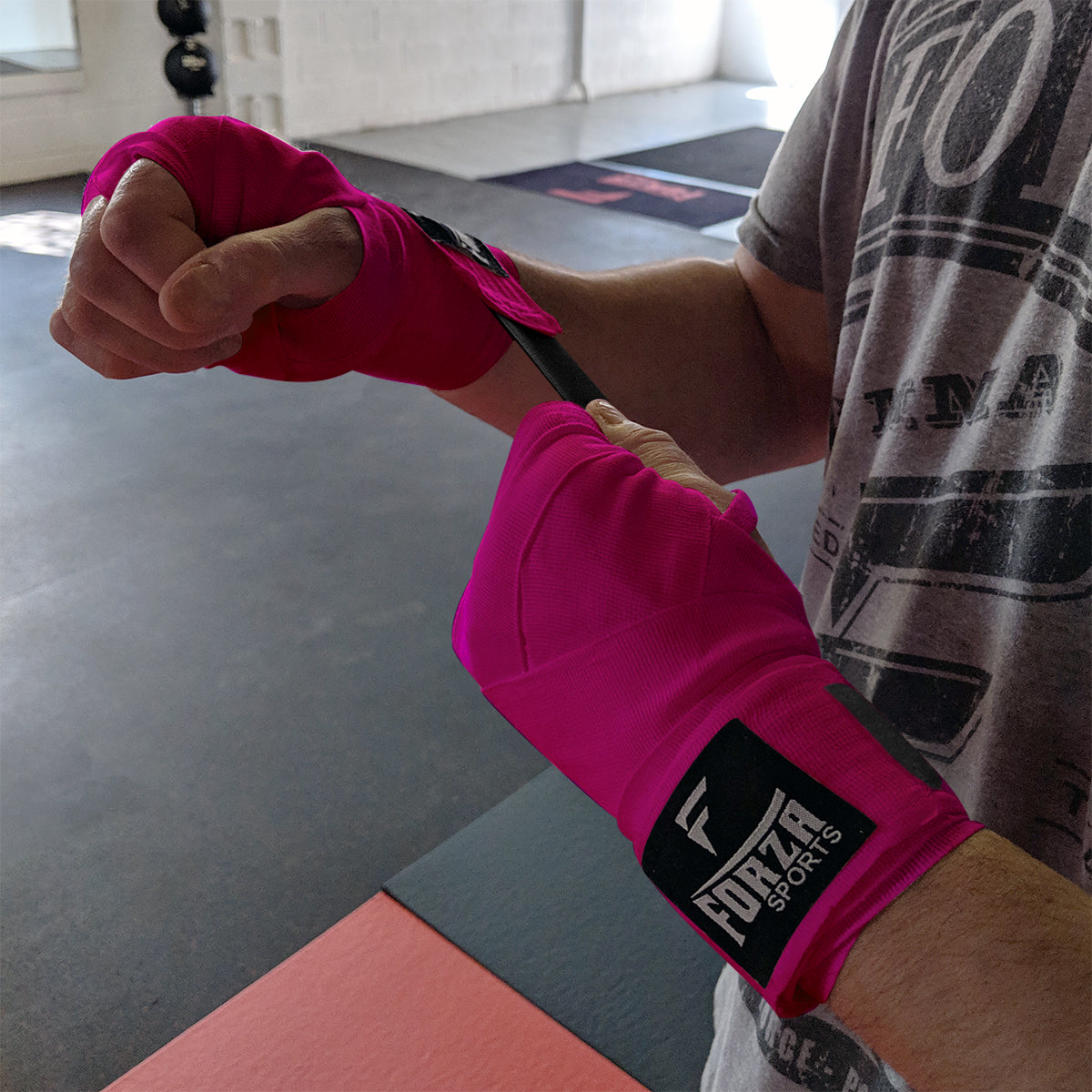 Person wrapping their fists with pink boxing wraps in a gym setting