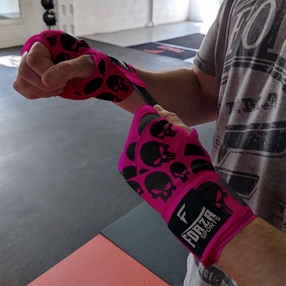 Person wearing pink boxing wraps with black skull designs in a gym setting