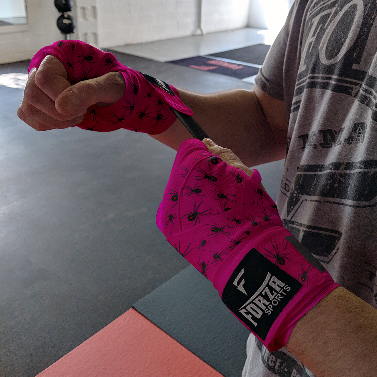 Person wearing pink boxing hand wraps with black spider design in a gym setting