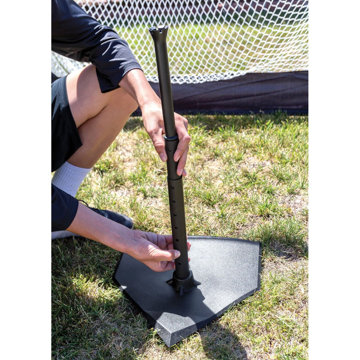 Person holding a black baseball training pop over a home plate on grass
