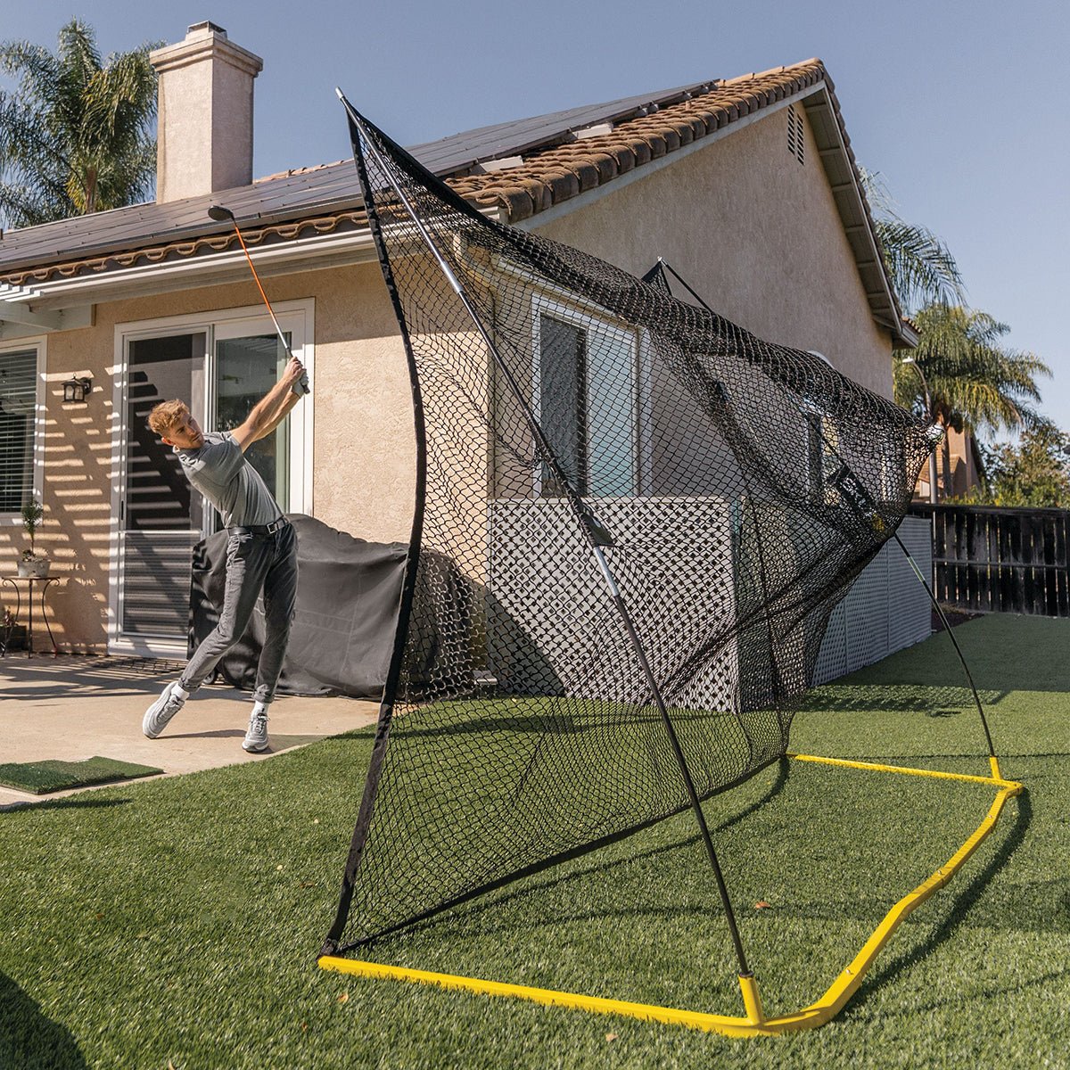 Person using a baseball practice golf net in a backyard
