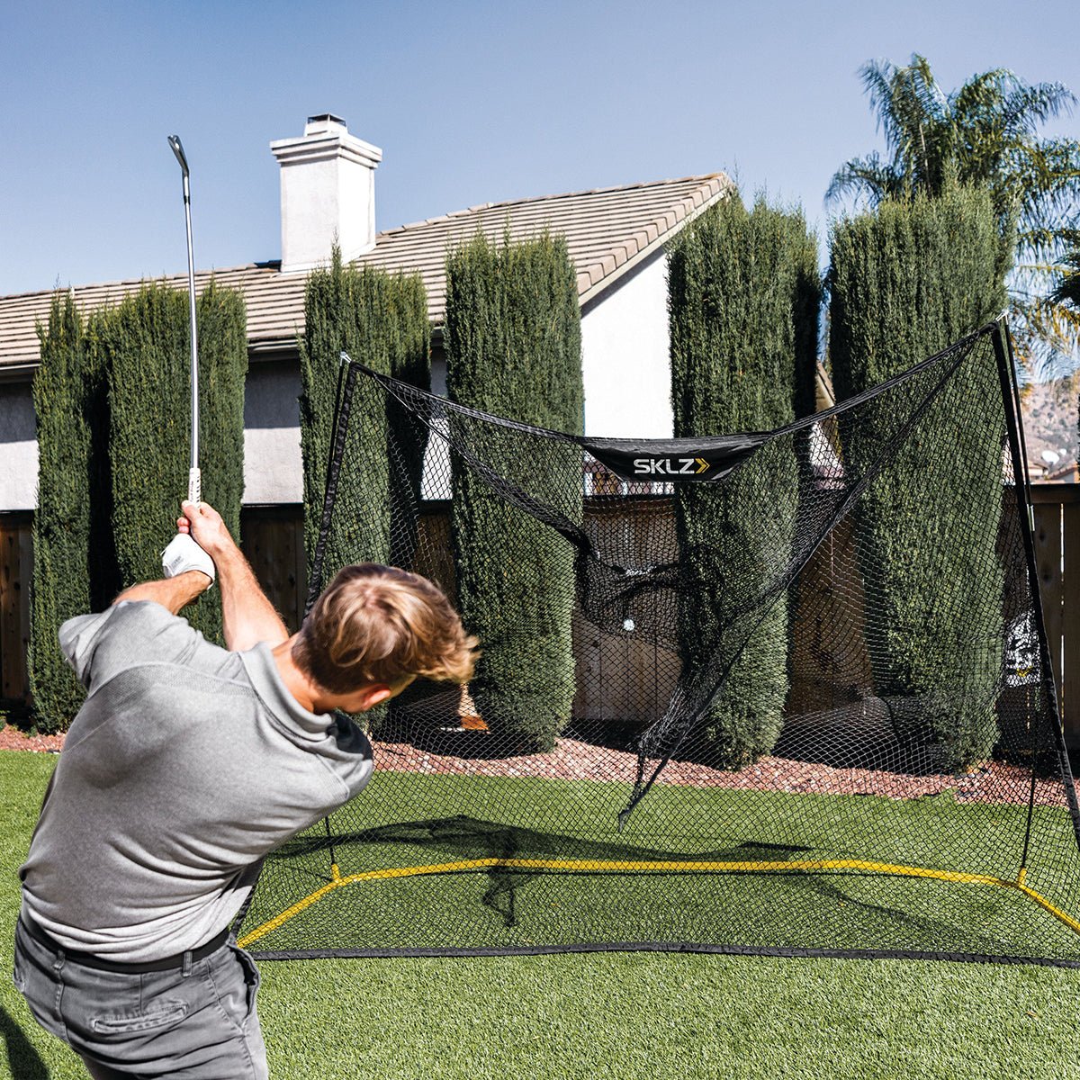 Person practicing golf net swings in a SKLZ golf net on a residential lawn.