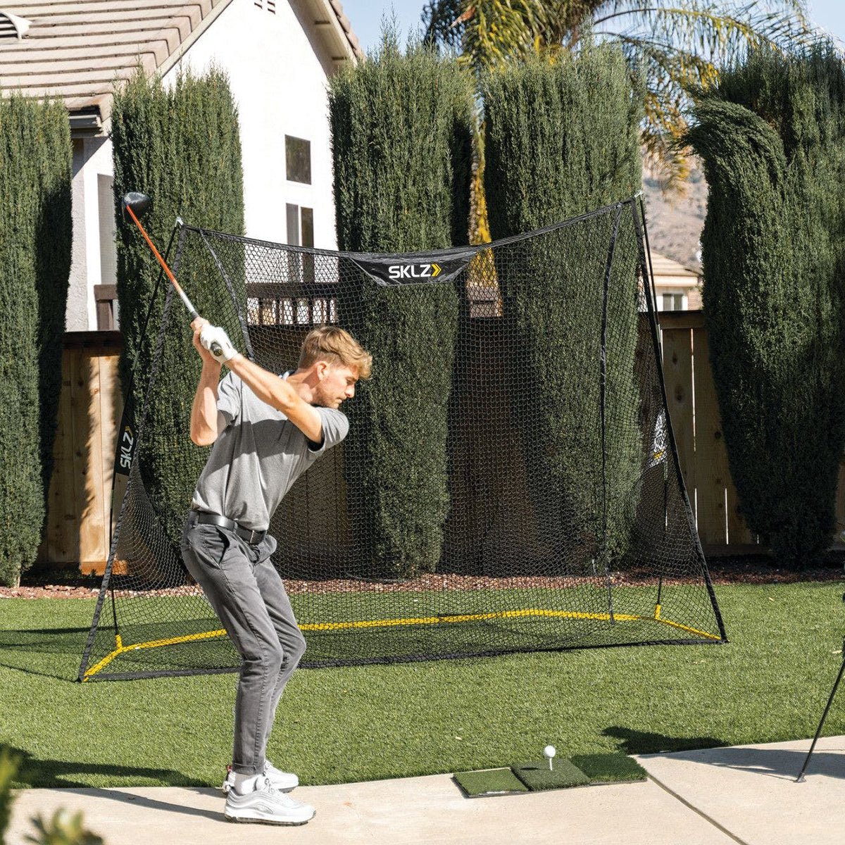 Person practicing golf net swings in a SKLZ golf net on a grassy area.