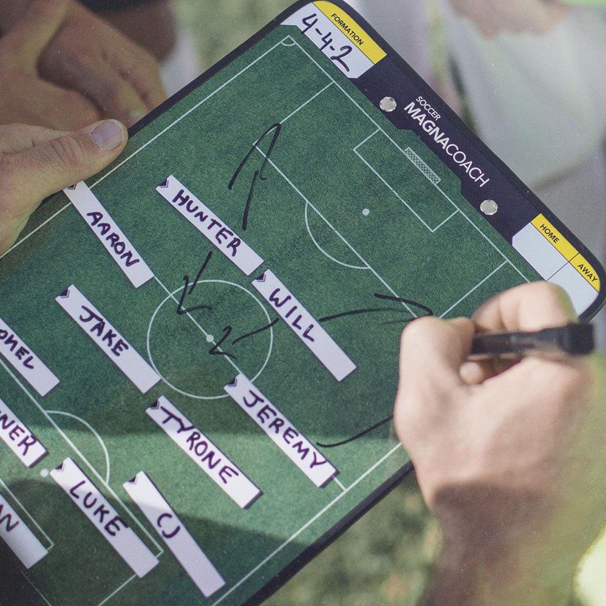 Person drawing a football play on a tactical dry erase board with names labeled