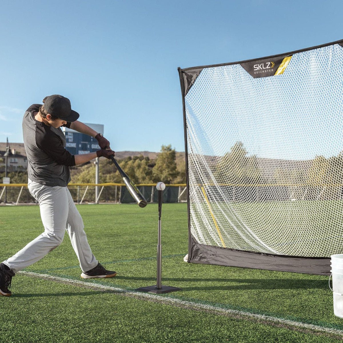 Person practicing batting baseball training aid in a sports facility with a SKLZ net and tee.