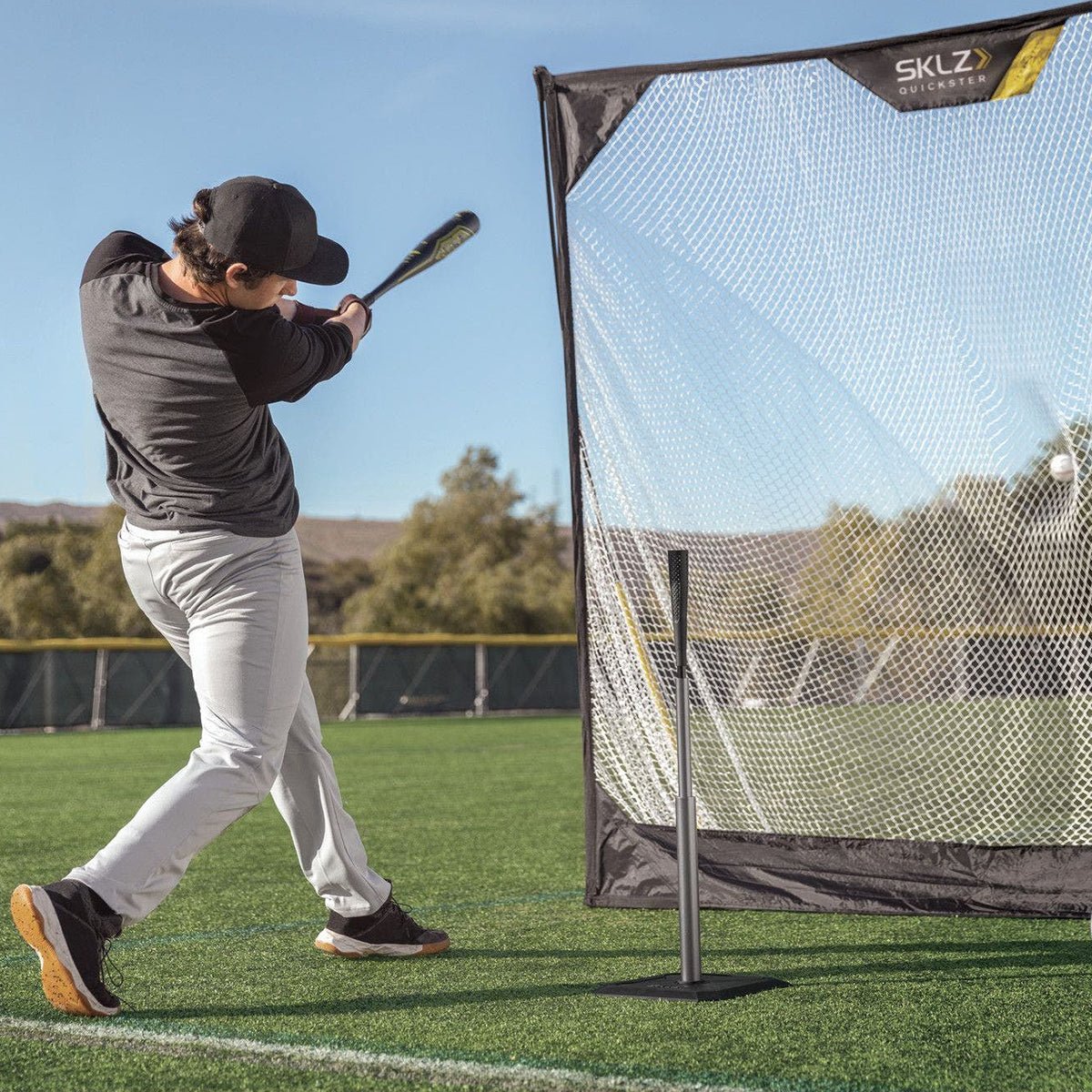 Person practicing baseball training aid swings in front of a SKLZ net on a field with.