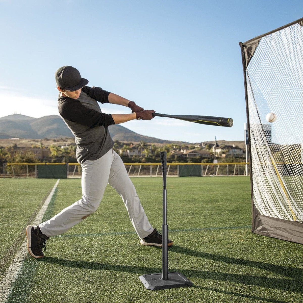 Person practicing baseball training aid swing with a netted hitting system on a field.