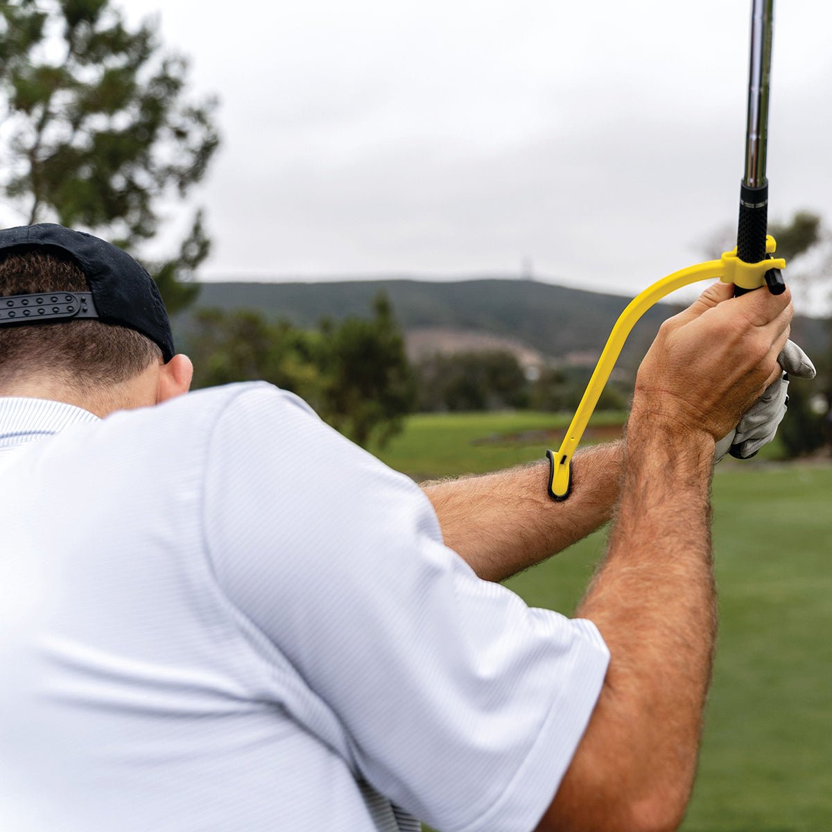 Person holding a golf club with a yellow golf swing trainer on a golf course