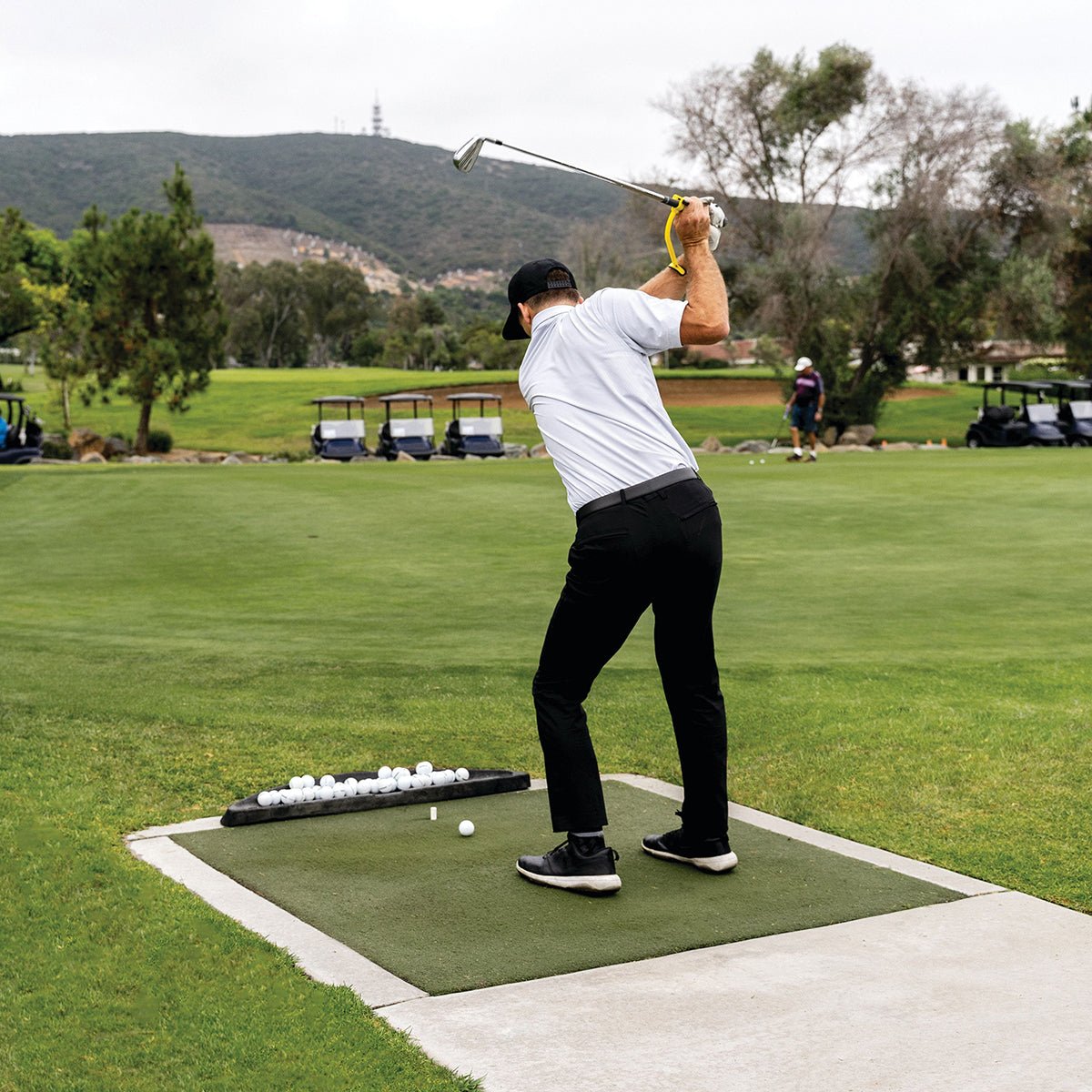 Person practicing golf swing trainer on a driving range with mountains in the background