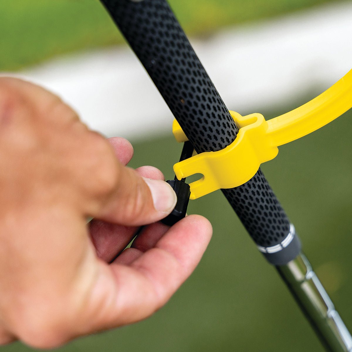 Hand using a yellow golf swing trainer to adjust a black fishing rod reel.