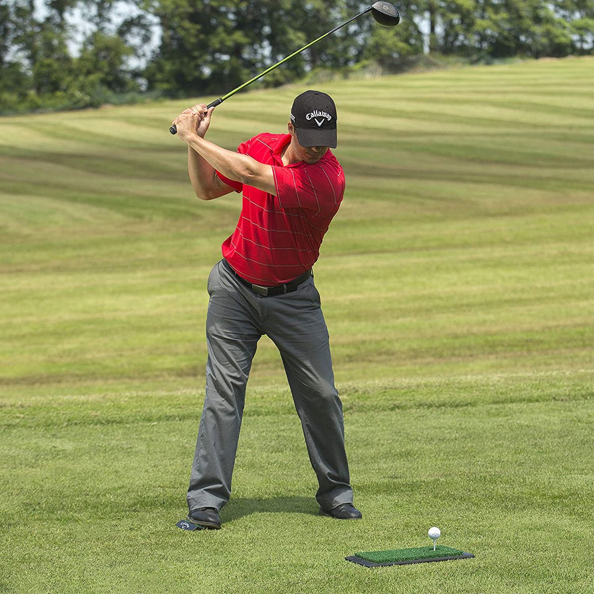 Man in red shirt and gray pants swinging a golf club on a green golf platform