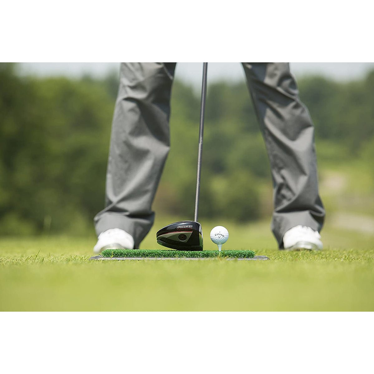Golf player about to hit a ball with a club on a green hitting golf mat.