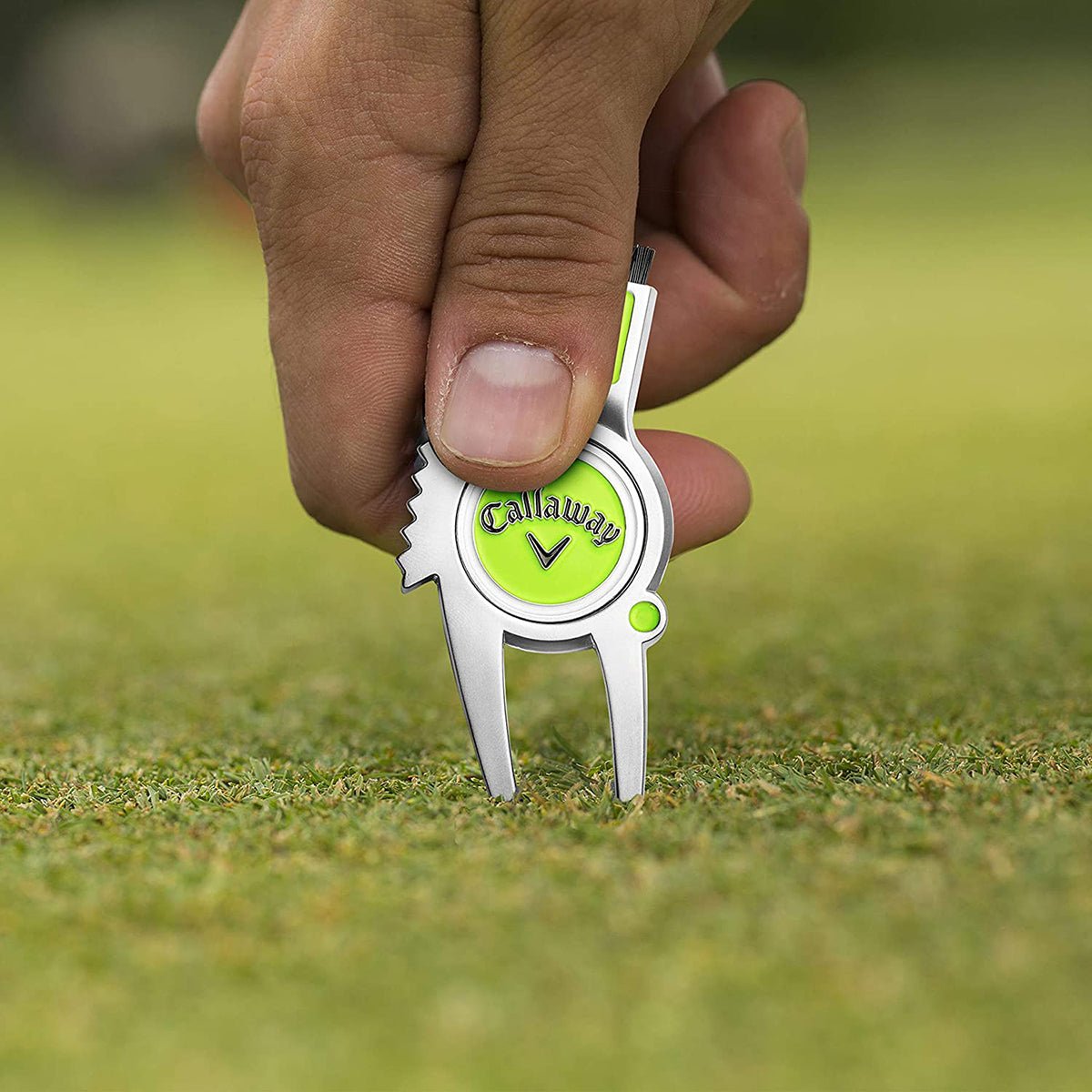 Callaway golf divot repair tool held by a hand on a grassy background