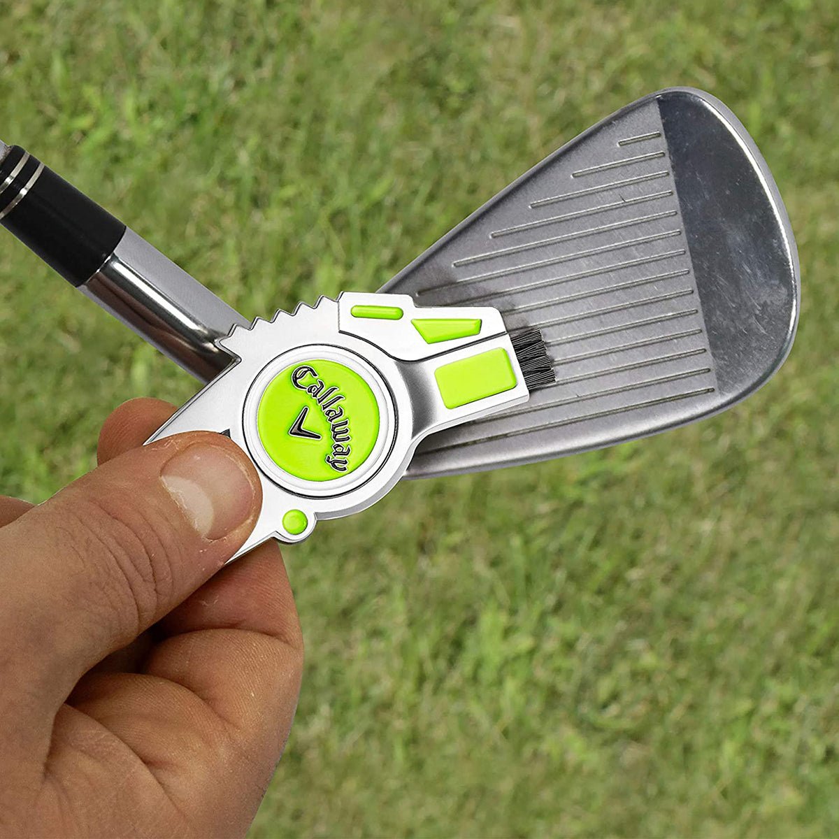 Golf divot repair tool with a green Callaway logo held by a hand on a grassy background