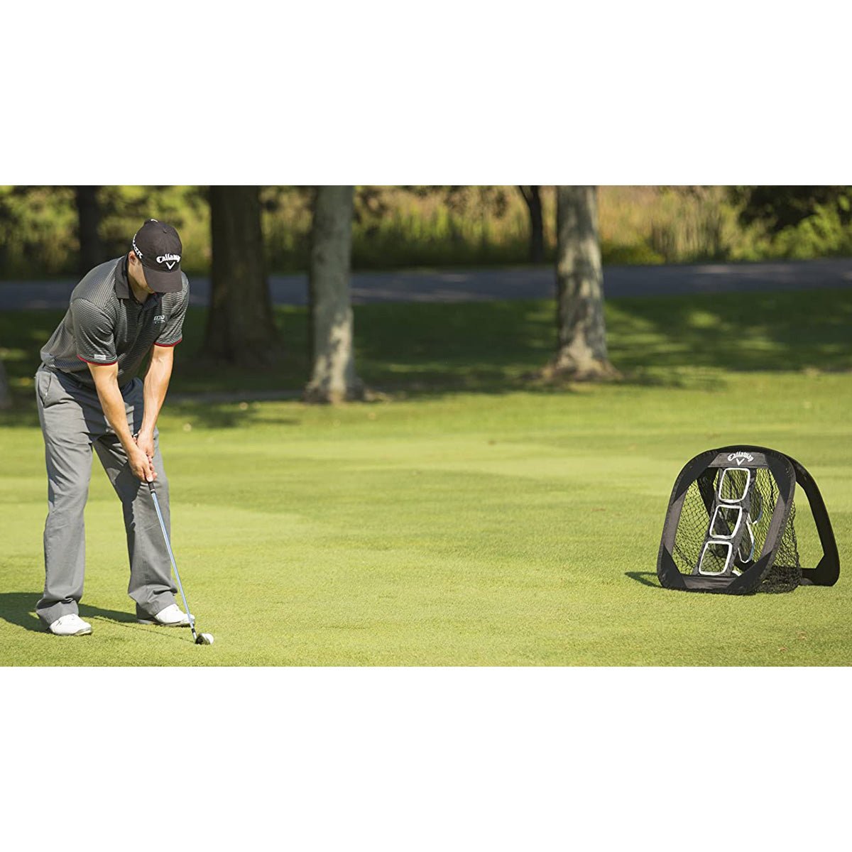 Person practicing golf chip shot net on a green field with a golf practice net in the background.