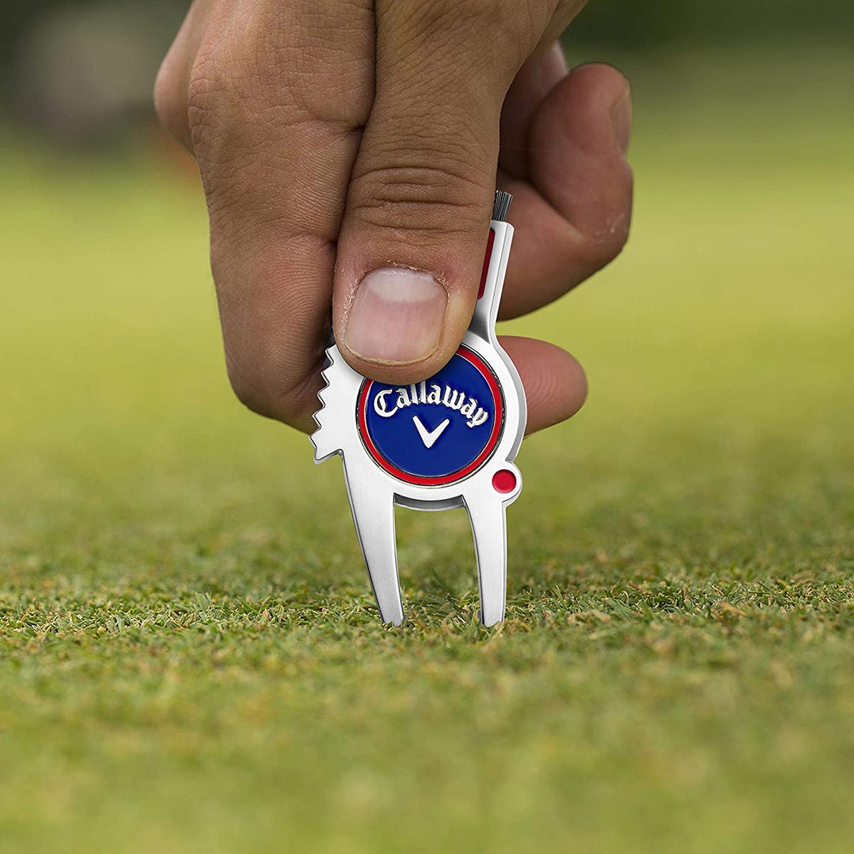 Callaway golf divot repair tool held by a hand on a grassy background