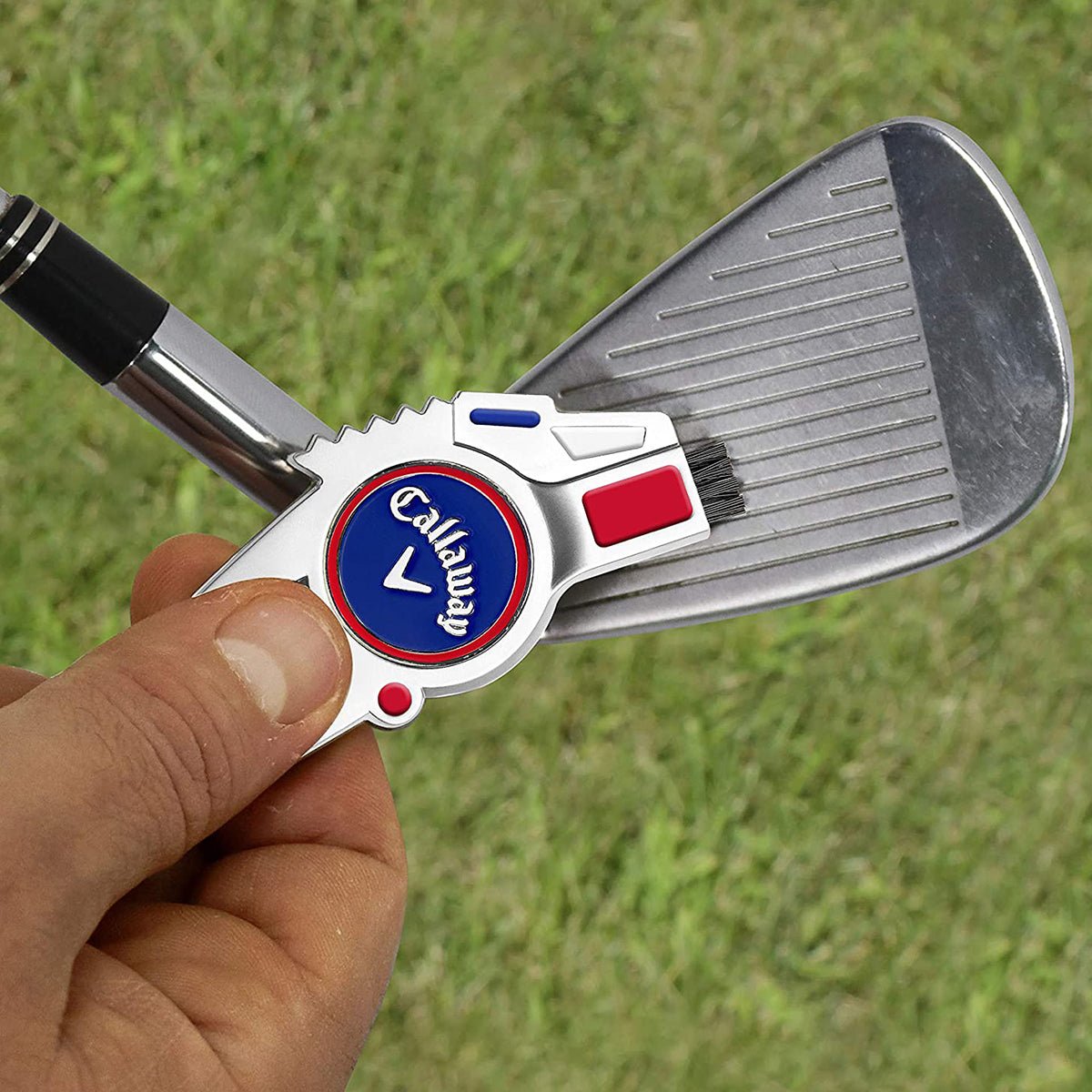 Golf divot repair tool with a Callaway logo held by a hand against a grassy background