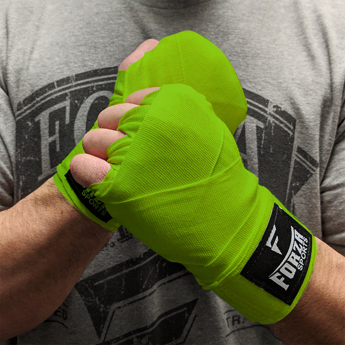Person wearing bright green boxing hand wraps with a brand logo, against a gray t-shirt background.