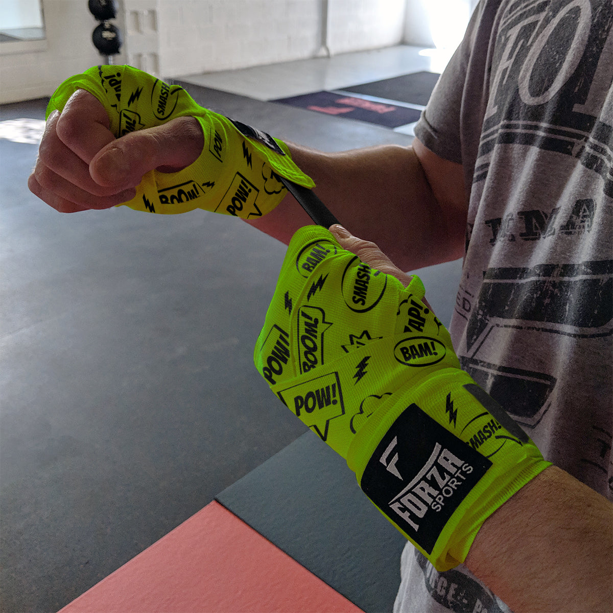 Person wearing bright green boxing hand wraps with black text, standing in a gym.