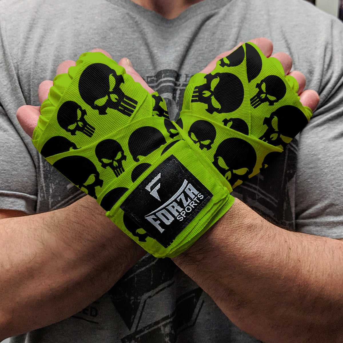 Green wrist wraps with black skull patterns held by a person wearing a gray shirt.
