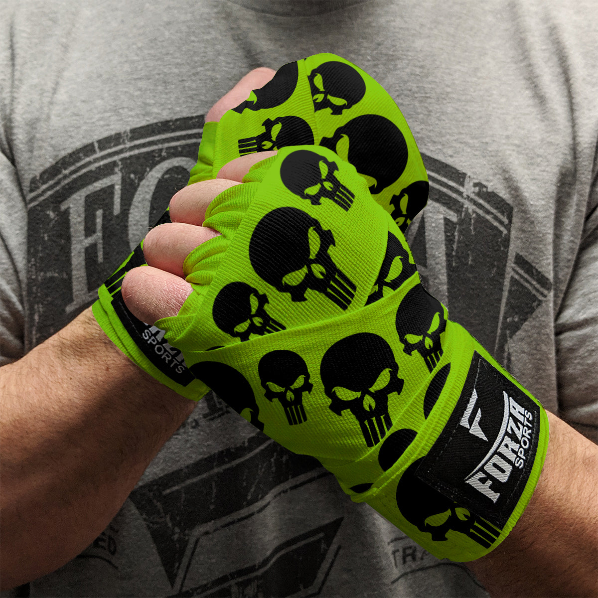 Green boxing hand wraps with black skull patterns worn by a person, against a gray t-shirt background.