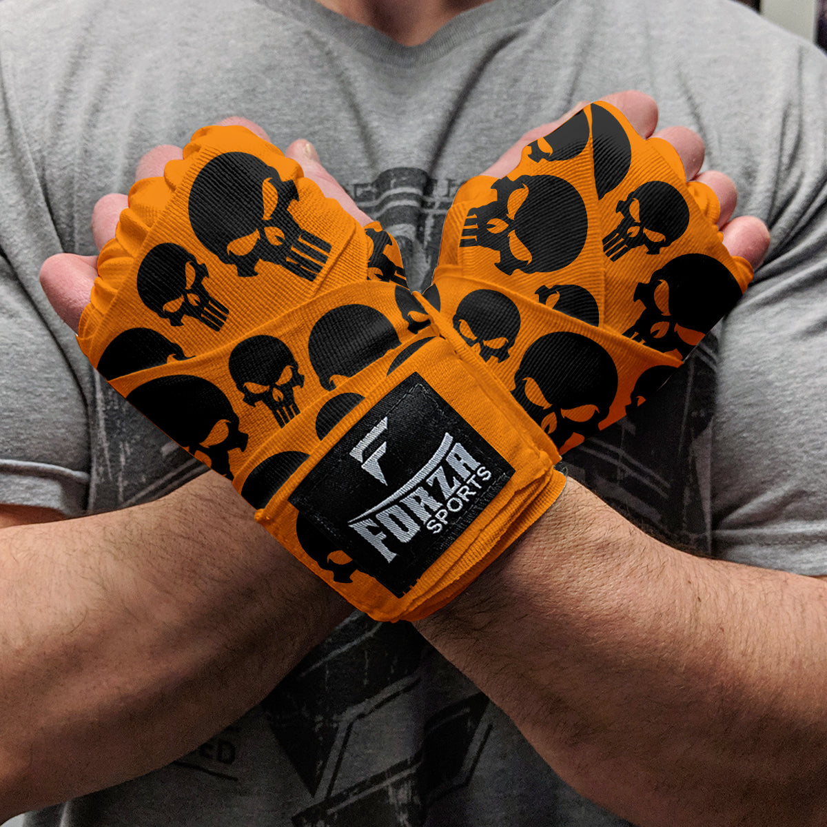 Orange wrist wraps with black skull patterns held by a person, branded 'Forza Sports'.