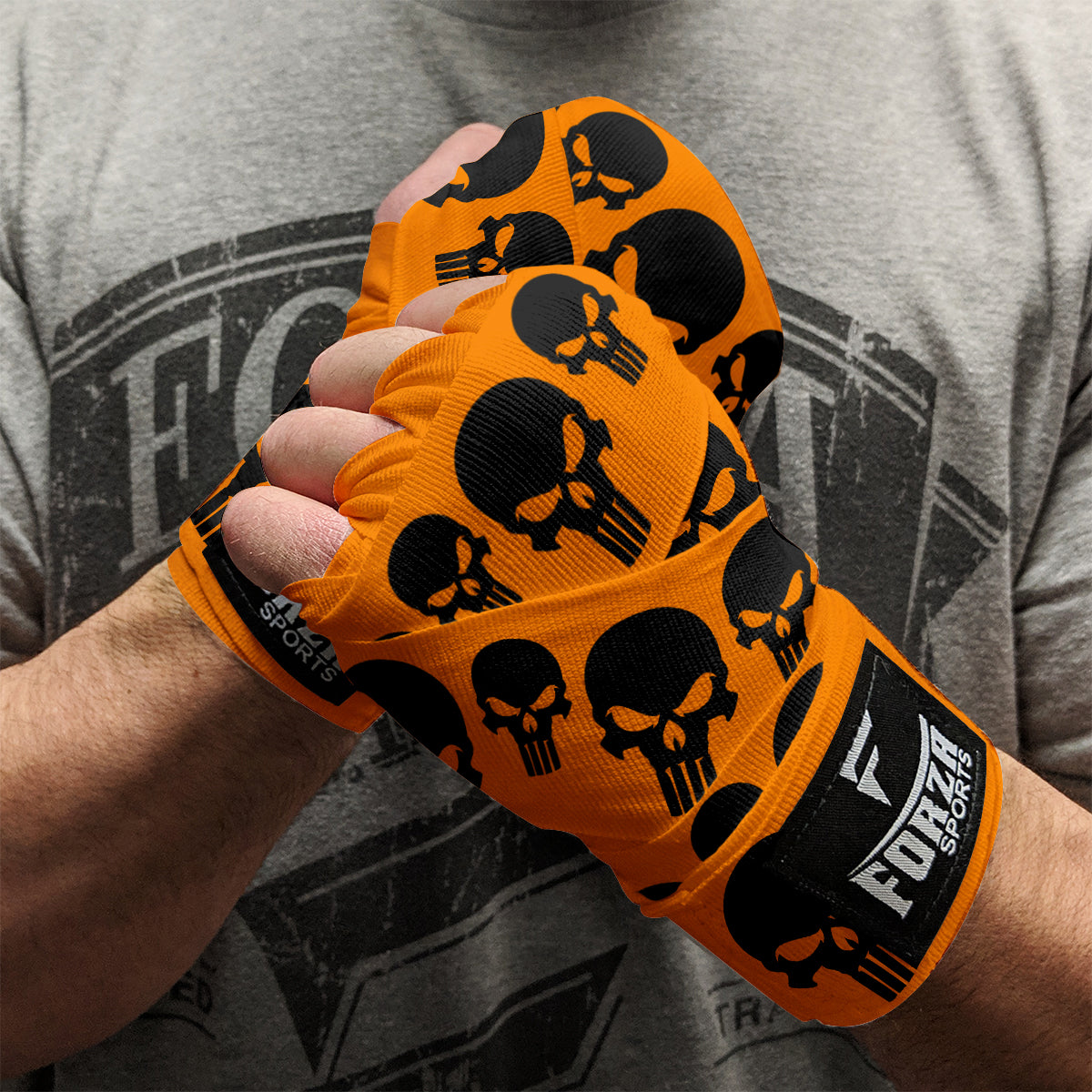 Orange boxing hand wraps with black skull designs on a person wearing a gray t-shirt.