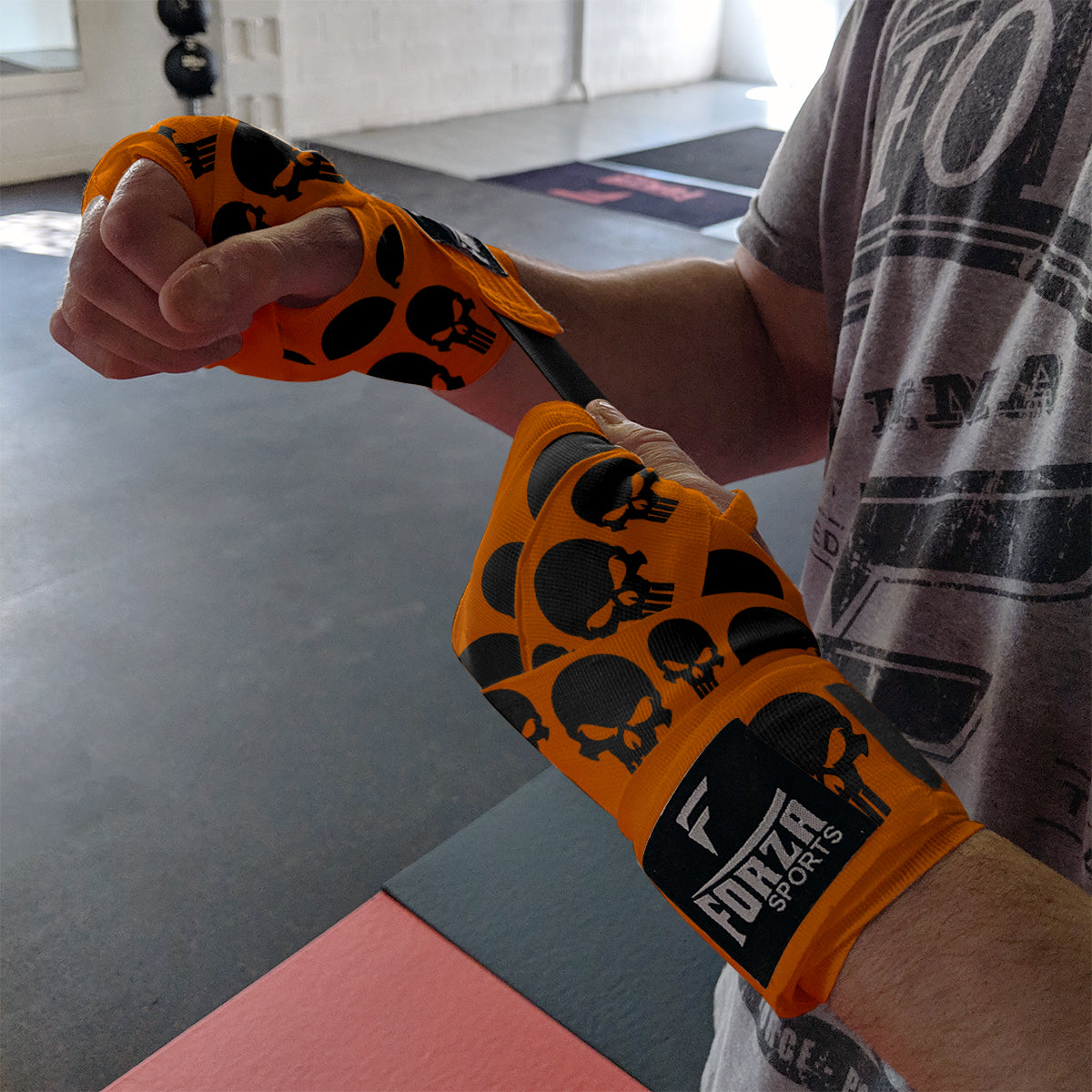 Person wearing orange boxing gloves with black skull patterns in a gym setting
