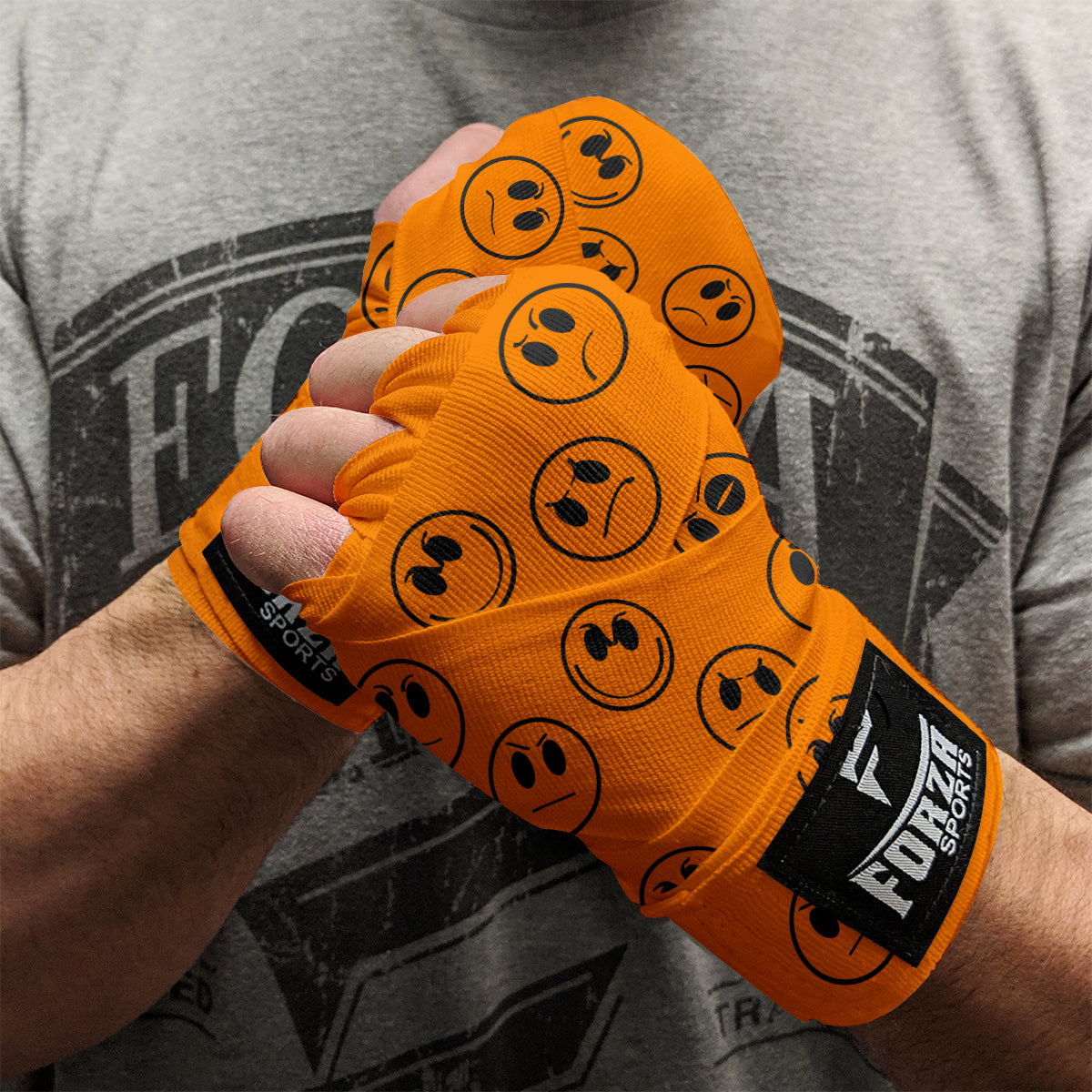 Orange boxing hand wraps with black smiley face patterns on a person wearing a gray t-shirt.