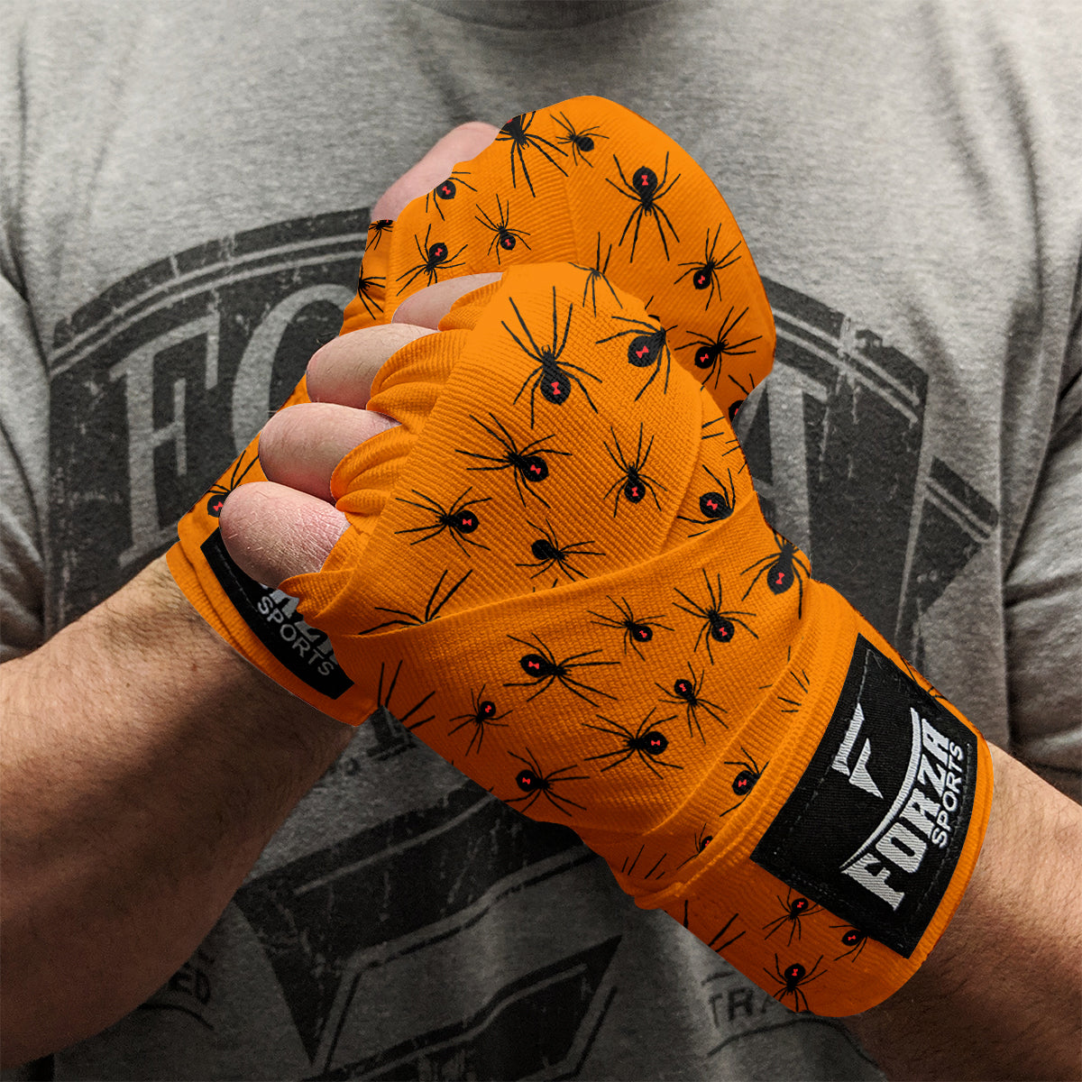Orange boxing gloves with black spider pattern worn by a person, against a gray t-shirt background.