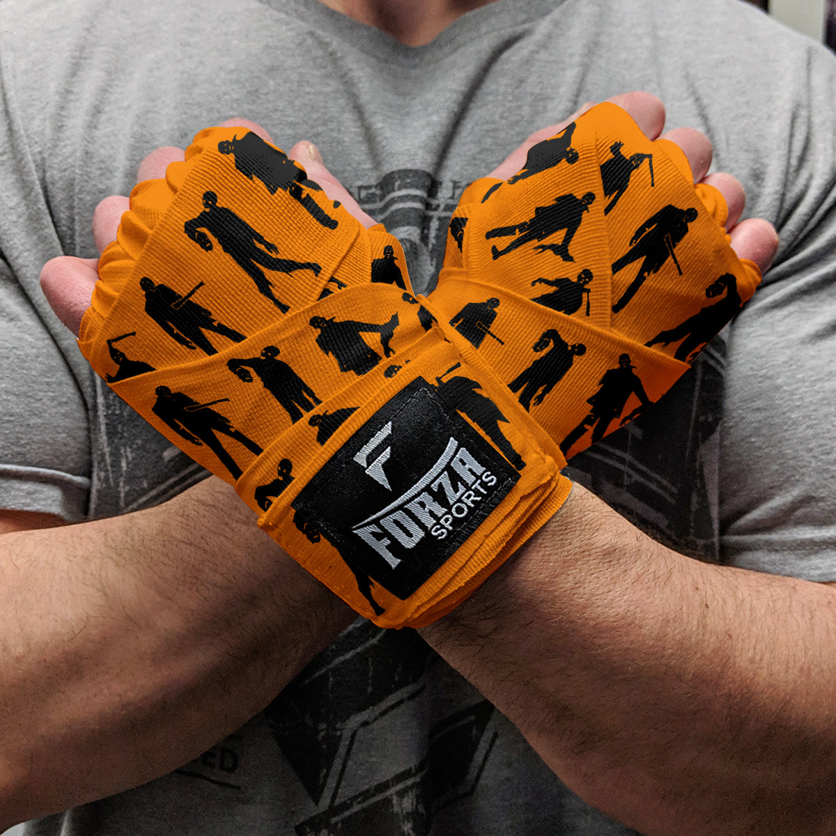 Orange wrist wraps with black silhouette designs held by a person wearing a gray shirt.