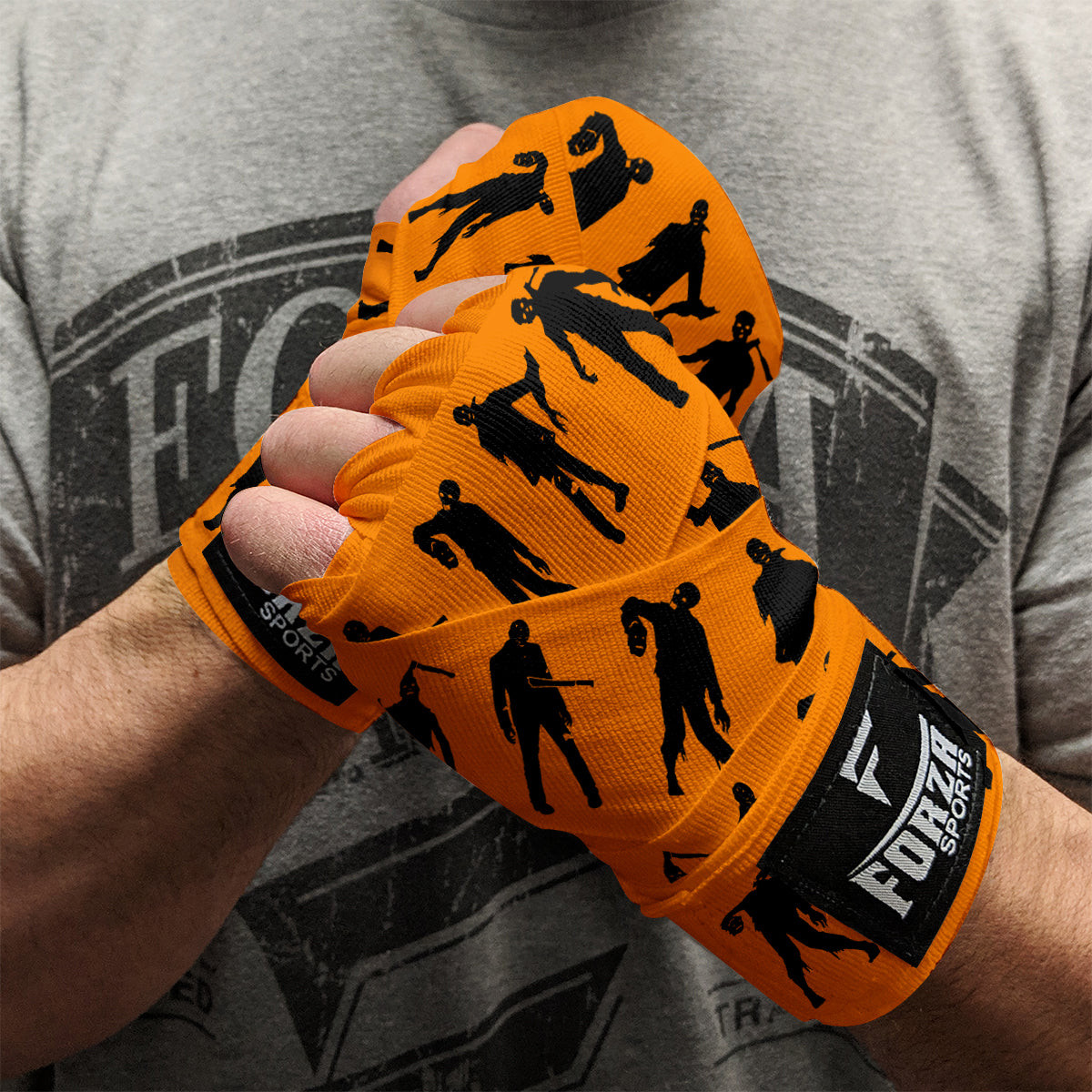 Orange boxing hand wraps with black silhouettes on a person wearing a gray t-shirt.