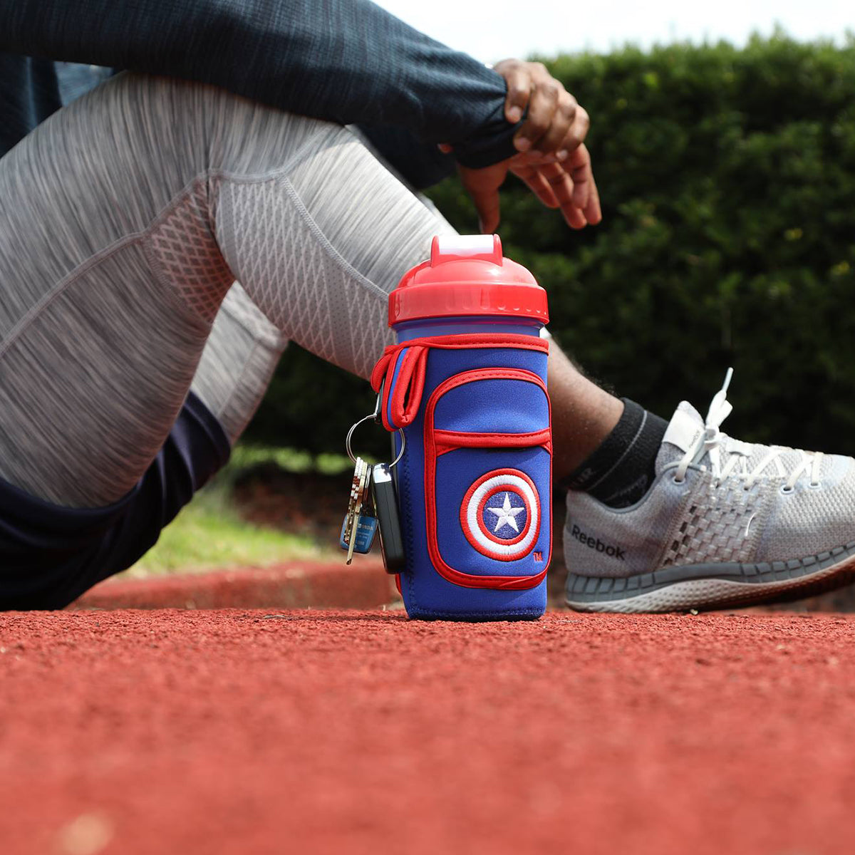Person sitting on a track with a Captain America water bottle and keys.